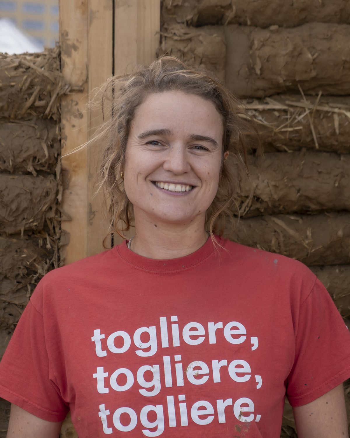 Laurane, fondatrice de Degré 47, souriante en t-shirt rouge devant un mur en terre et paille