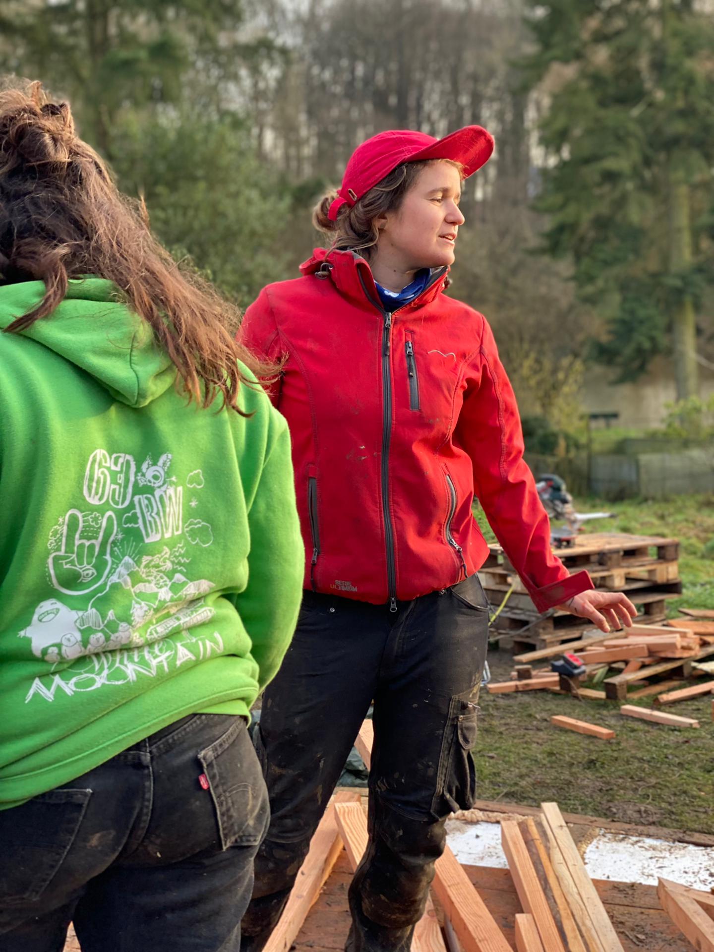 Deux femmes échangent sur un chantier, l'une en veste rouge, penchées l'une vers l'autre dans une discussion attentive.