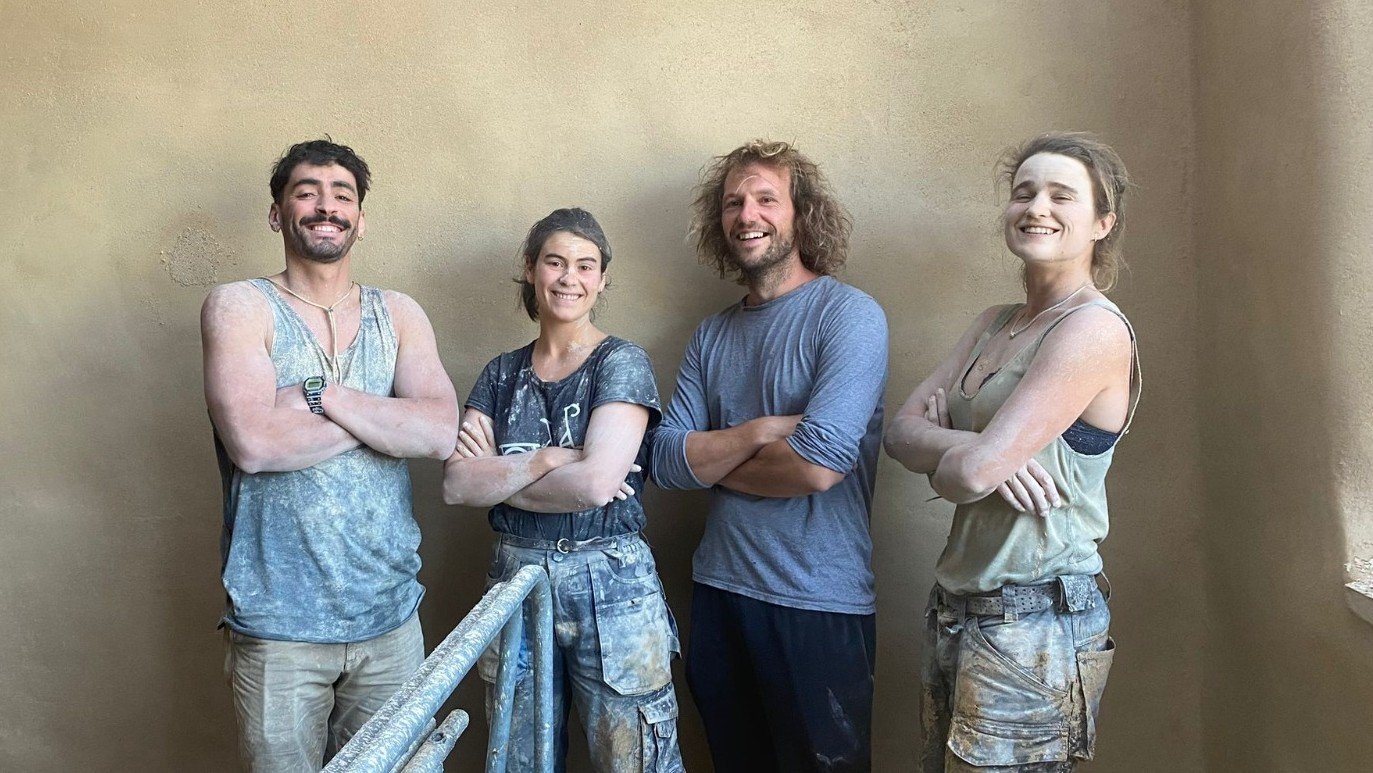 Laurane et son équipe, en tenue de chantier, devant un mur en enduit terre qu’ils viennent de réaliser