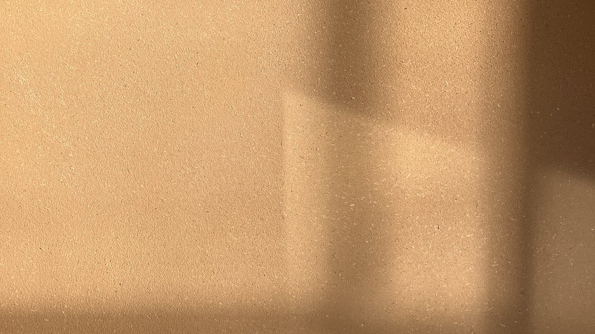 Mur en enduit terre ocre, l’ombre douce d’une fenêtre glisse sur la surface finie