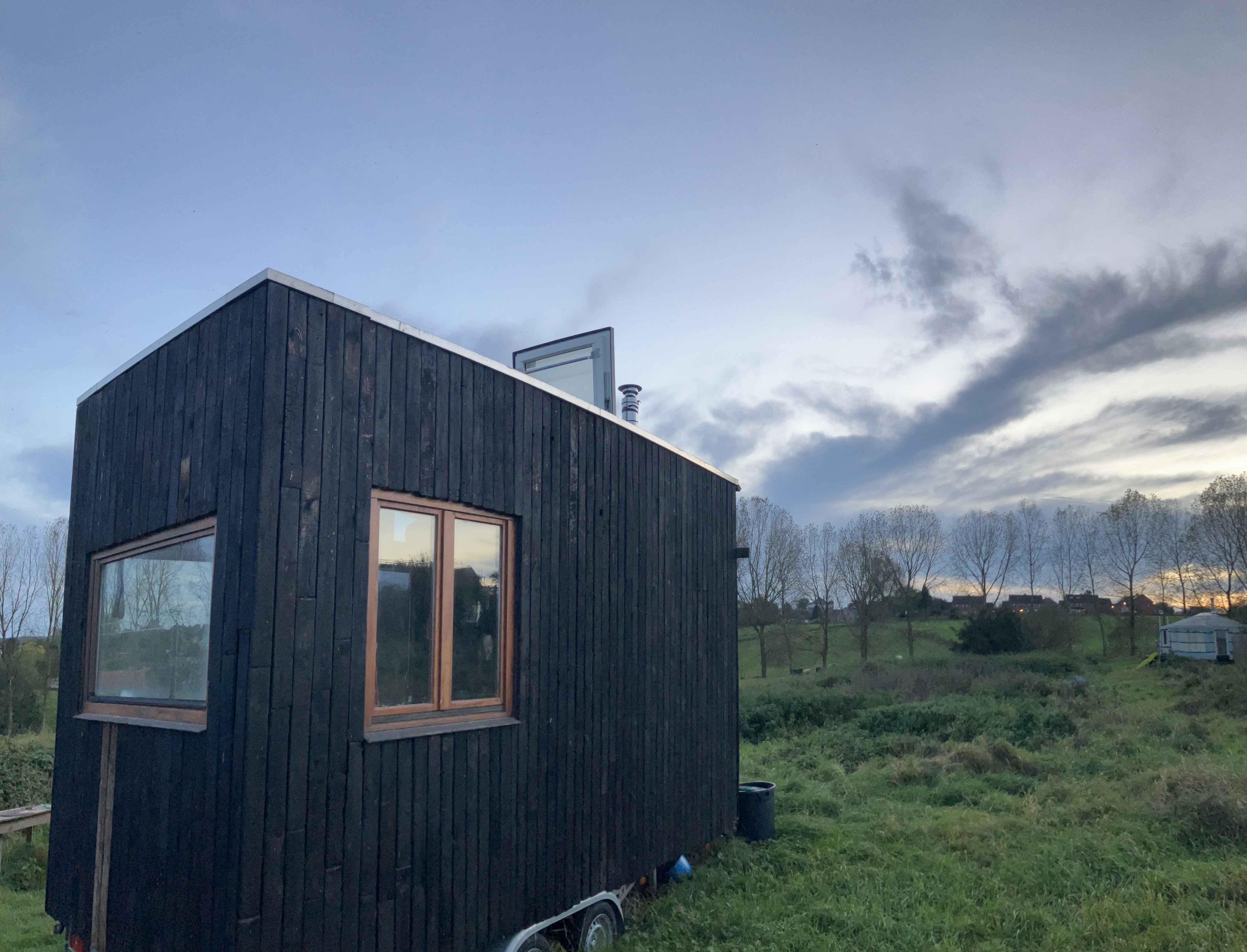 Tiny house terminée au bardage bois foncé, posée dans un pré au soleil