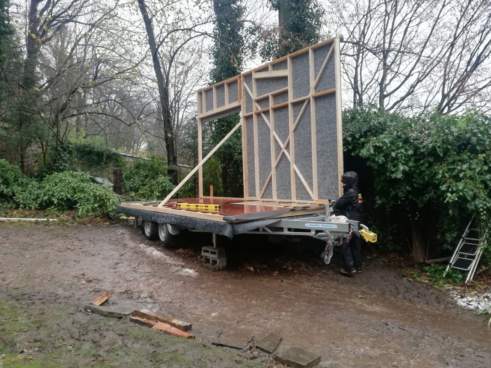 Premier mur de la tiny house dressé sur sa remorque, sur un terrain boueux