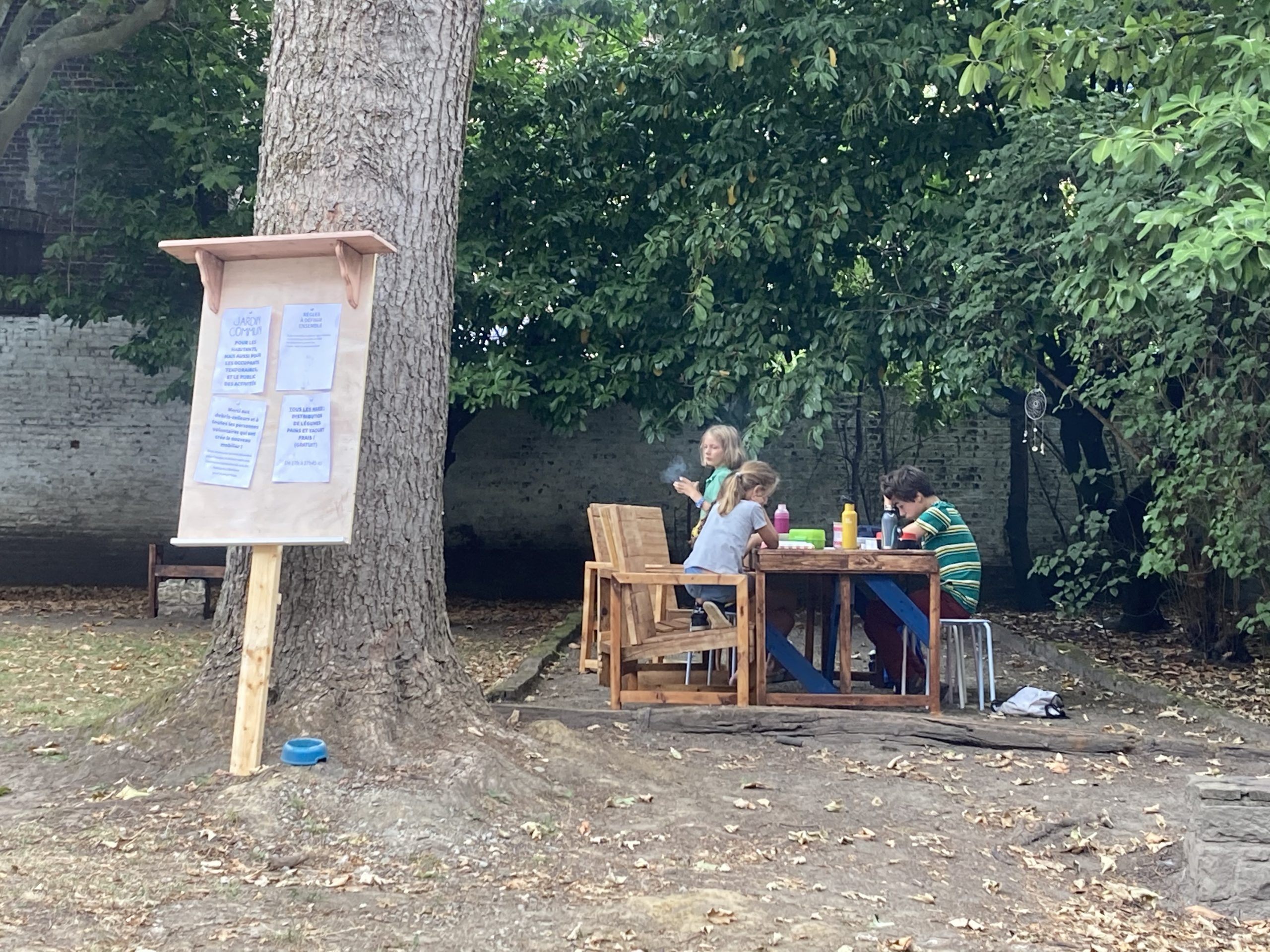 Personnes attablées dans le jardin près du panneau d'affichage