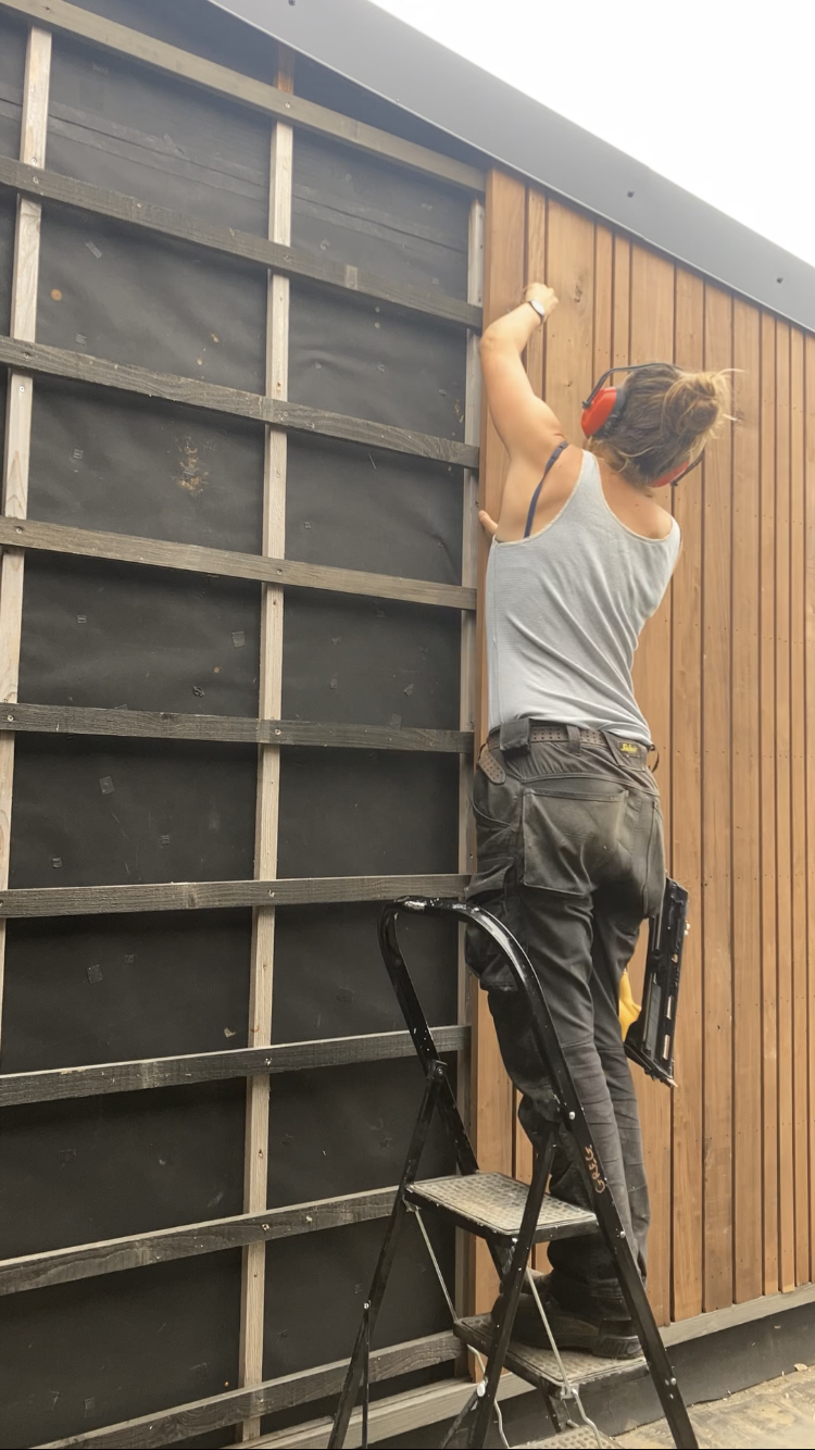 Un participant pose le bardage en hauteur, monté sur un escabeau