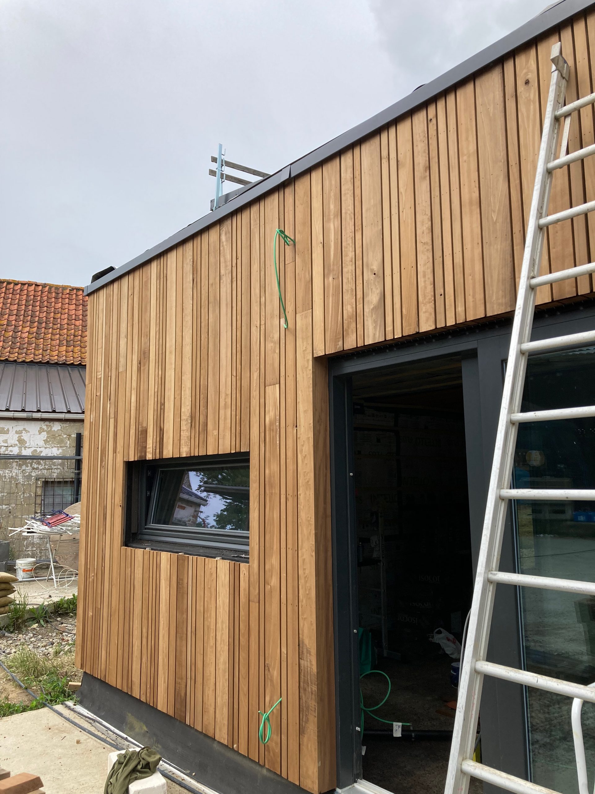Pan de façade bardé de bois autour d'une baie, échelle appuyée