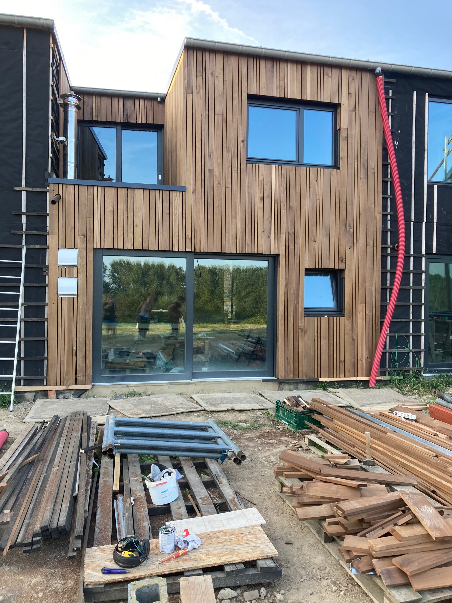 Maison bardée de bois presque terminée, bois de chantier au premier plan