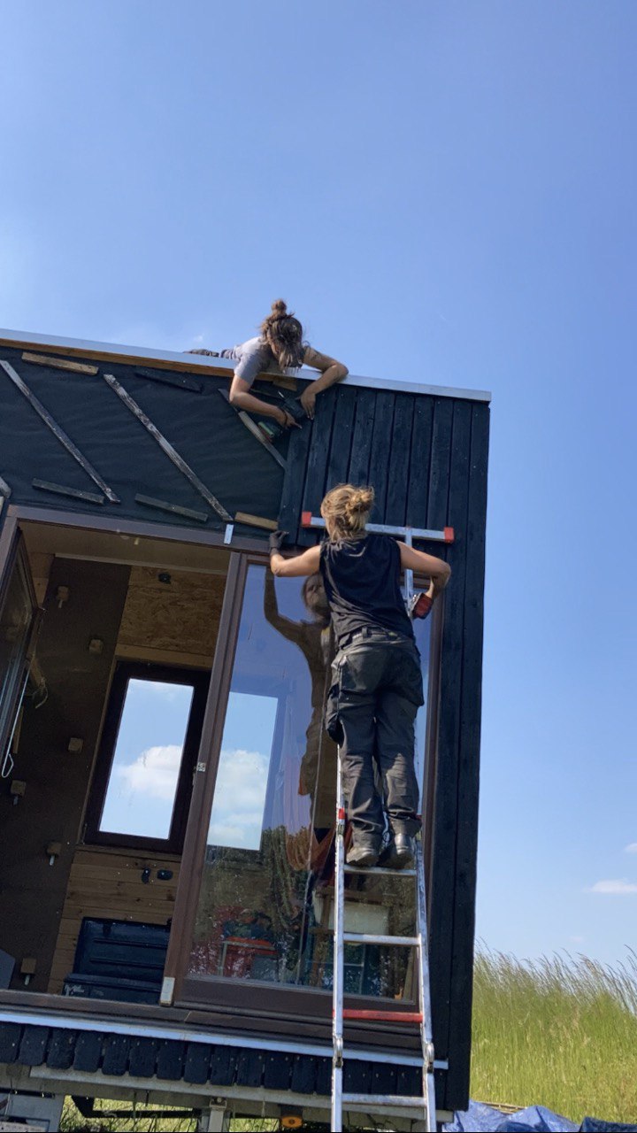 Un participant fixe le bardage noir sur le flanc du bâtiment