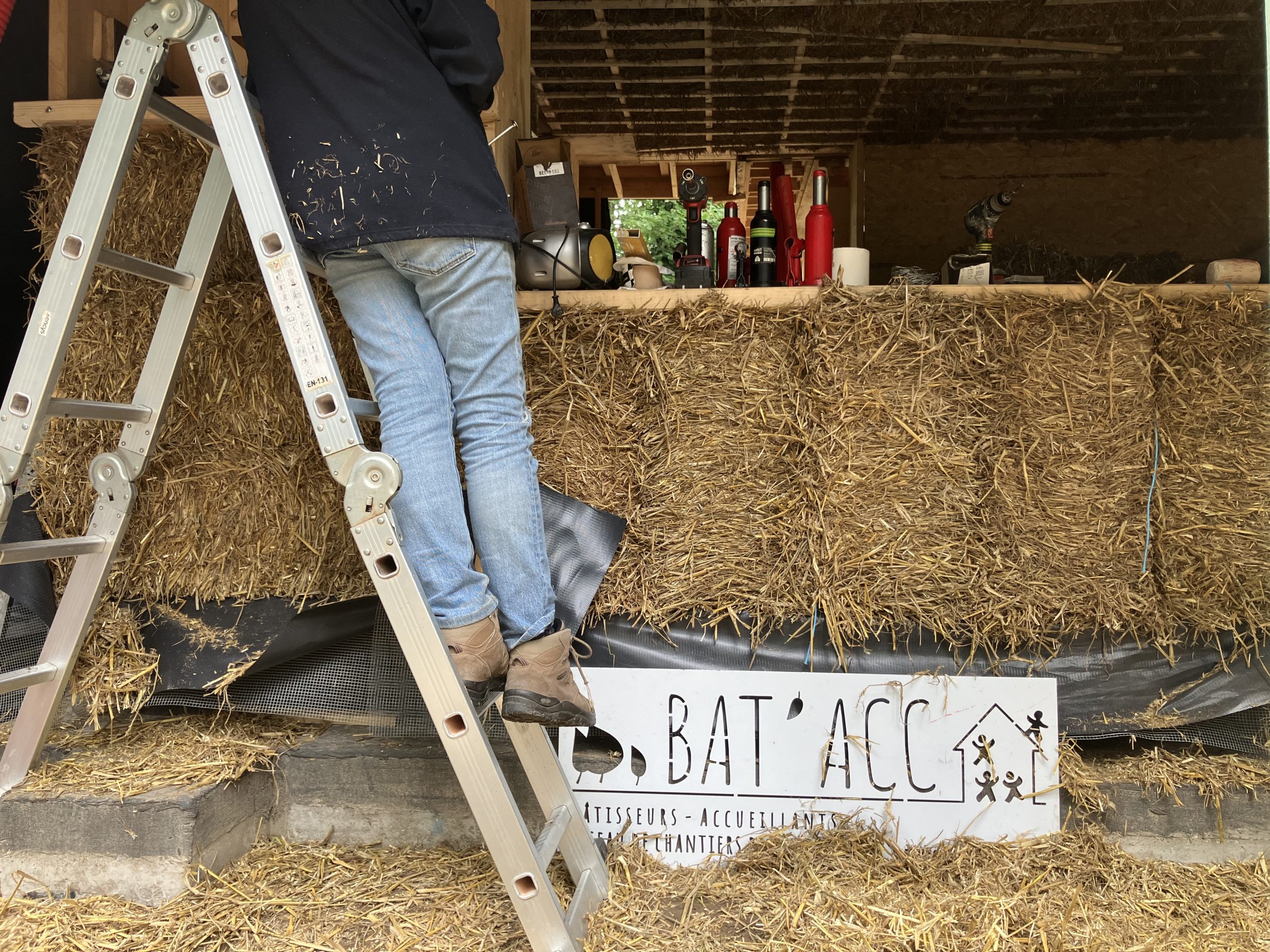 Un participant grimpe à l'échelle le long d'un mur en ballots de paille