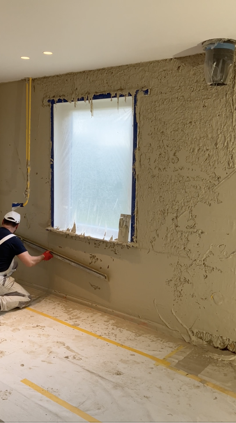 Un participant enduit le bas d'un mur autour d'une fenêtre, protections au sol