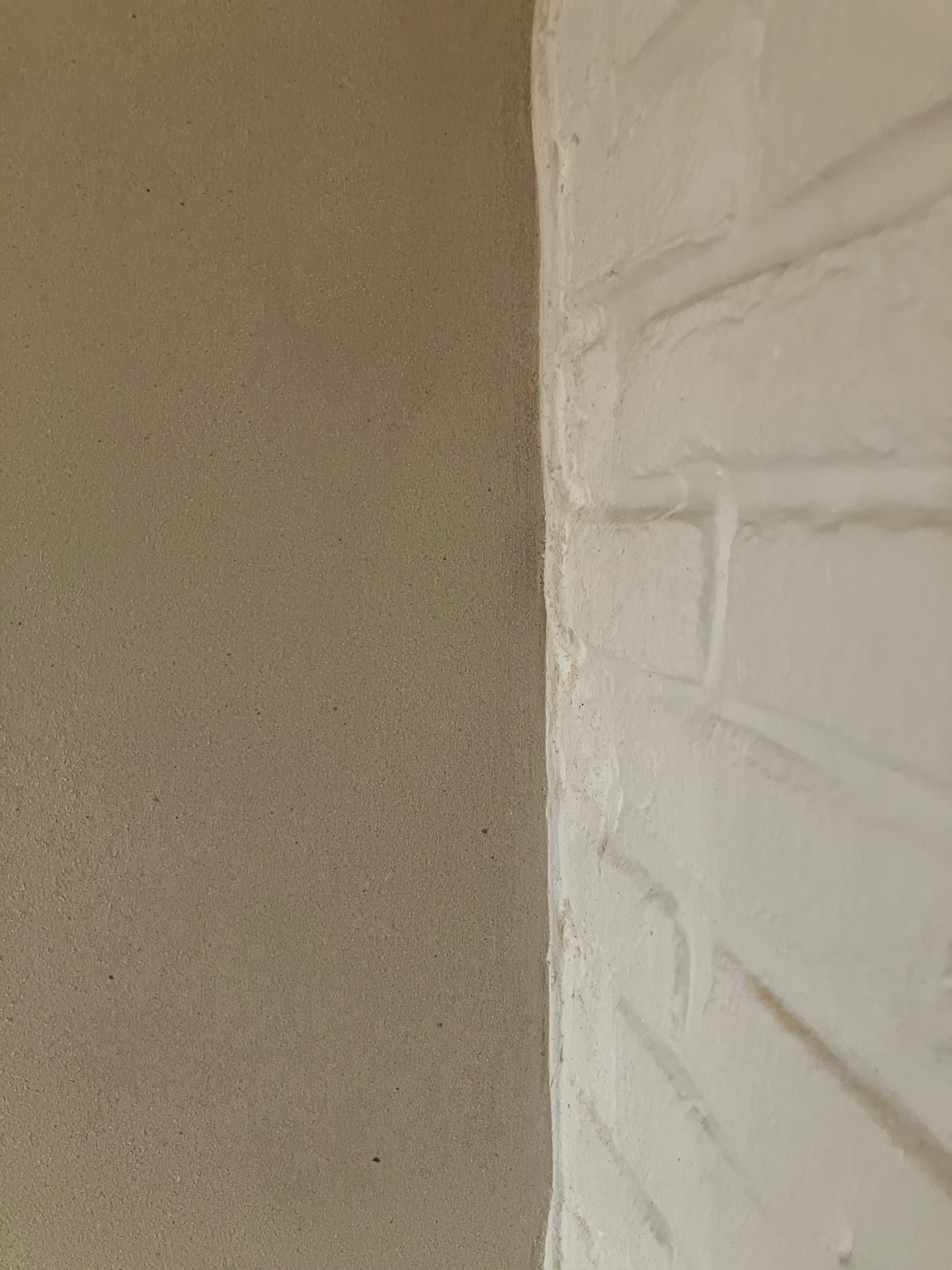 Détail d'un angle de mur en briques en partie recouvert d'enduit à la chaux