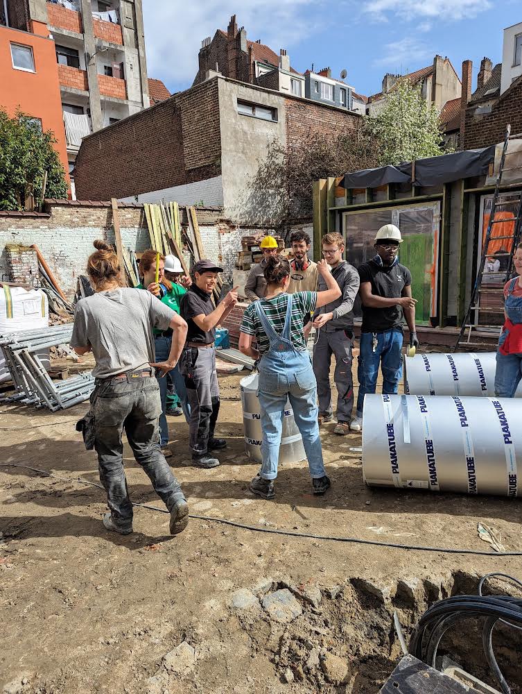Groupe de participants au pied du chantier, sacs de chaux et bâches vertes
