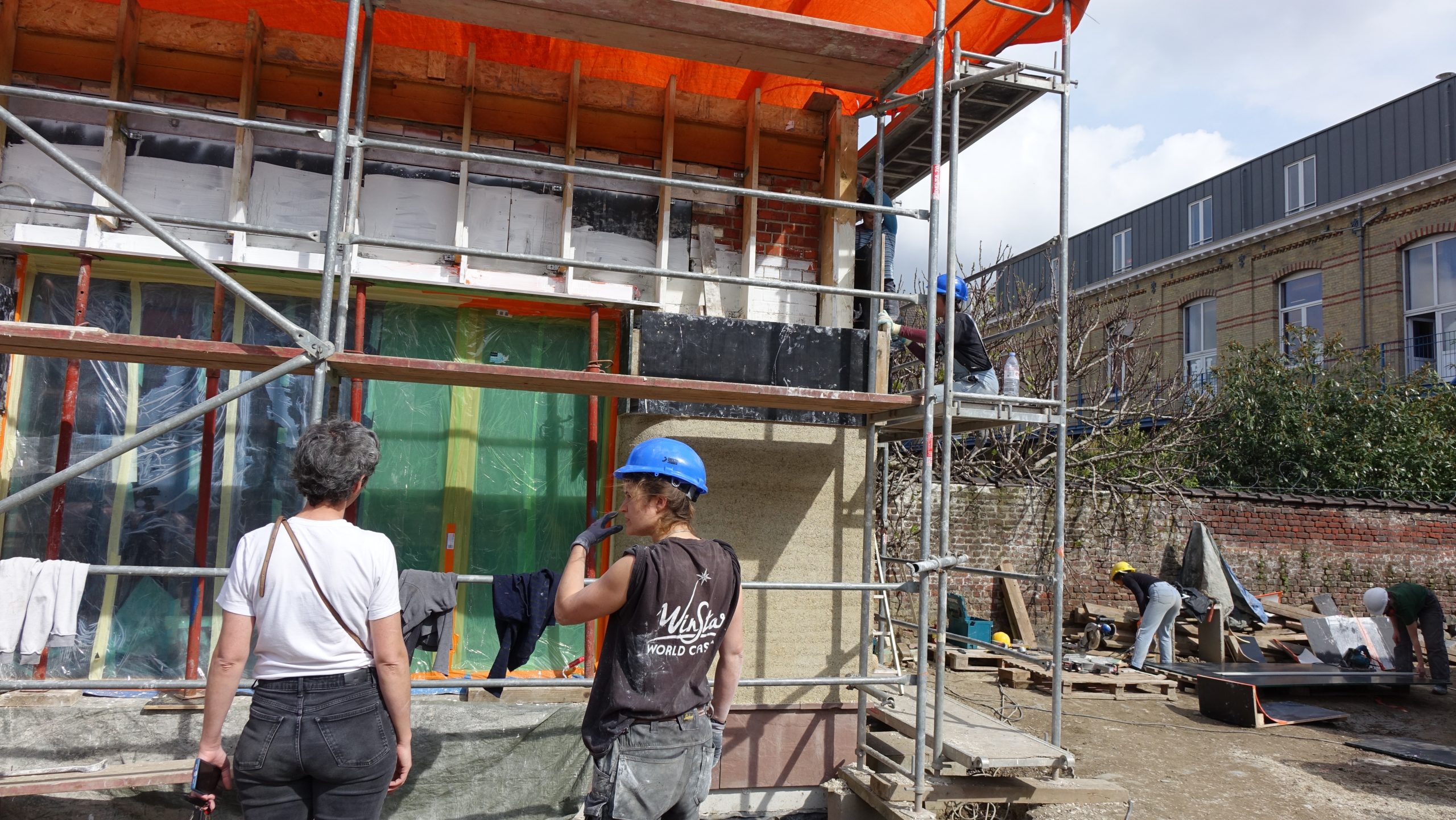 Participants sur l'échafaudage devant la façade bâchée de vert