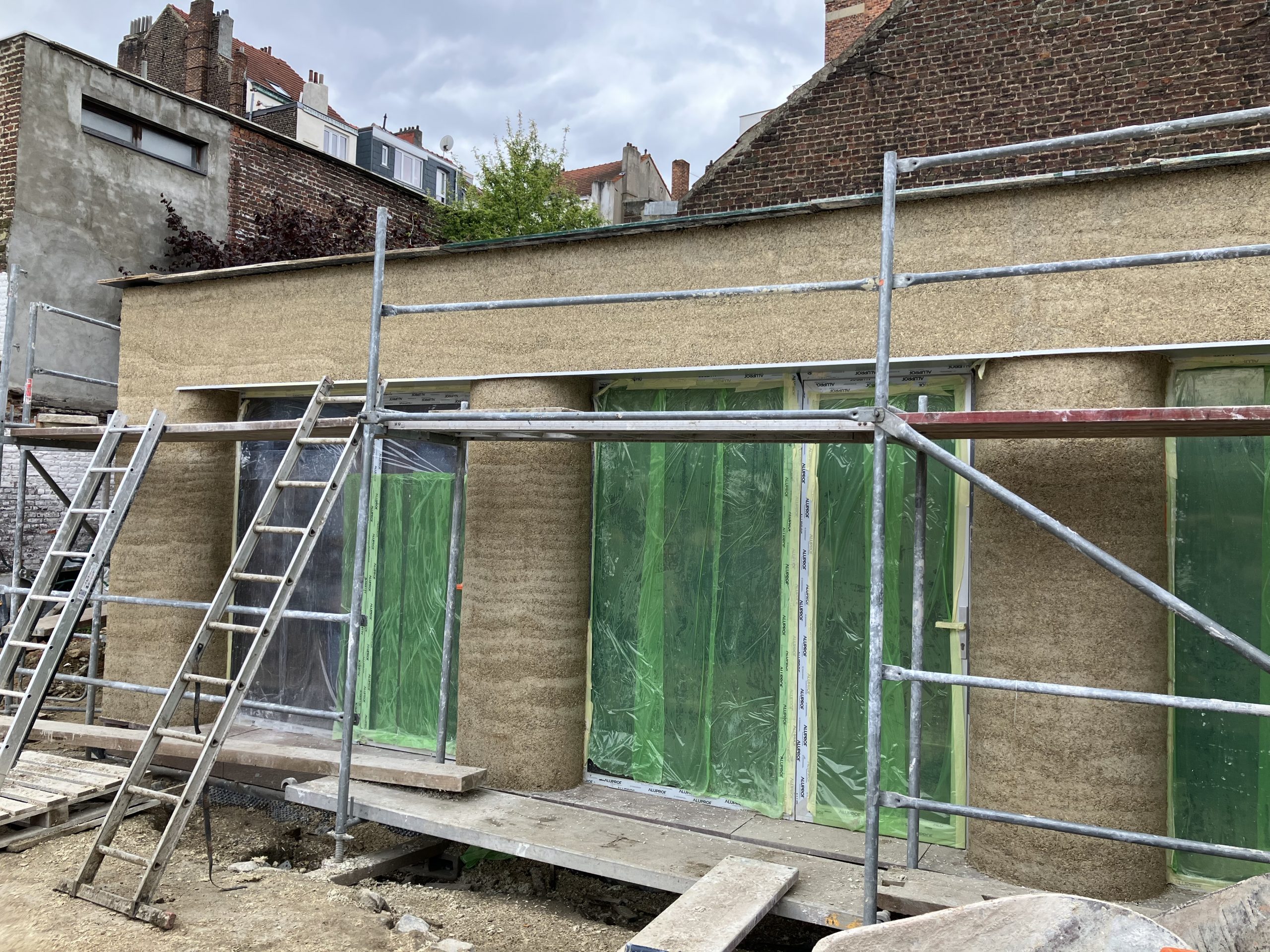 Façade en chaux-chanvre le long de l'échafaudage, bâches vertes