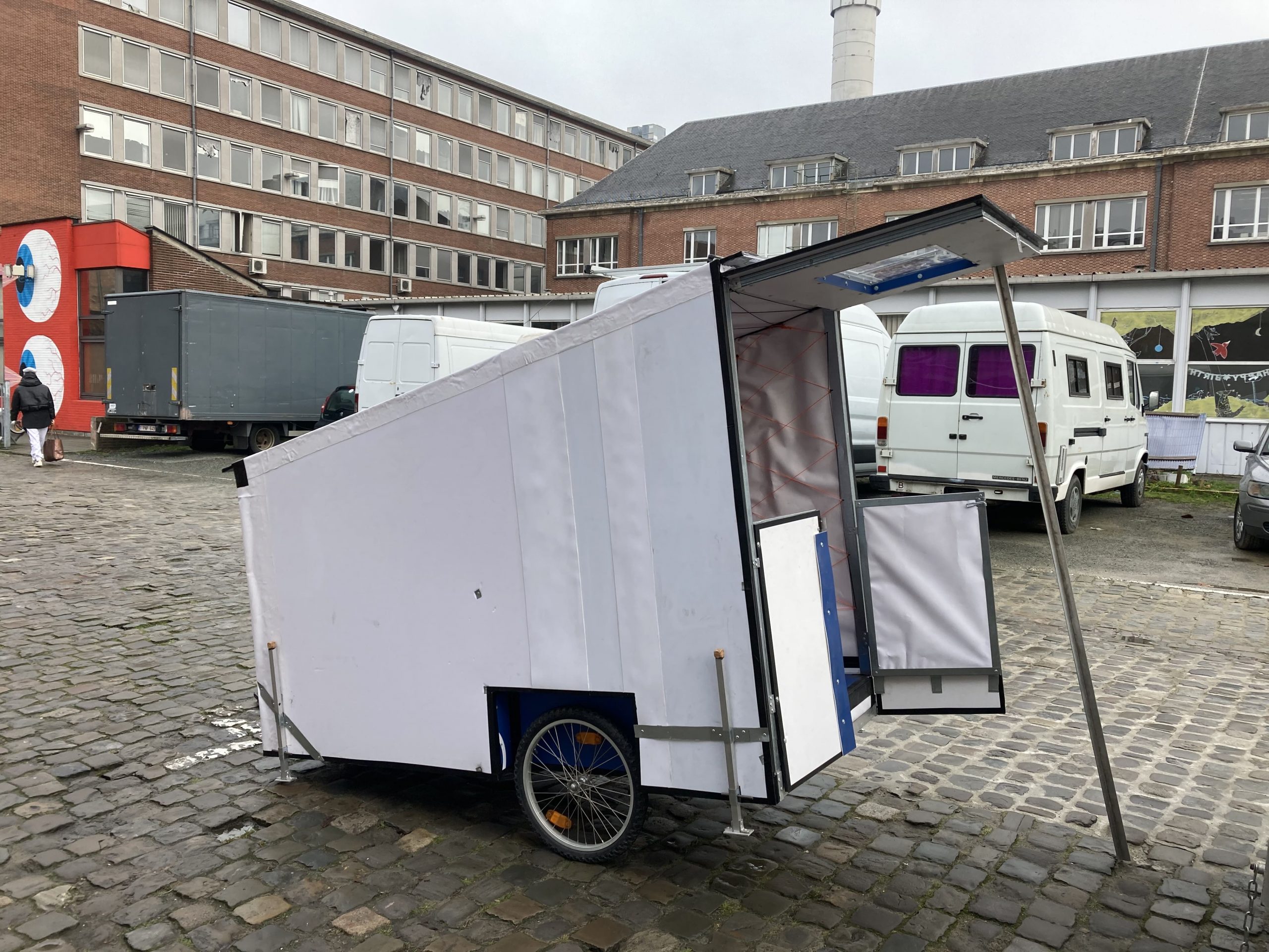 Habitat mobile blanc sur remorque, attelé pour un vélo, sur une place