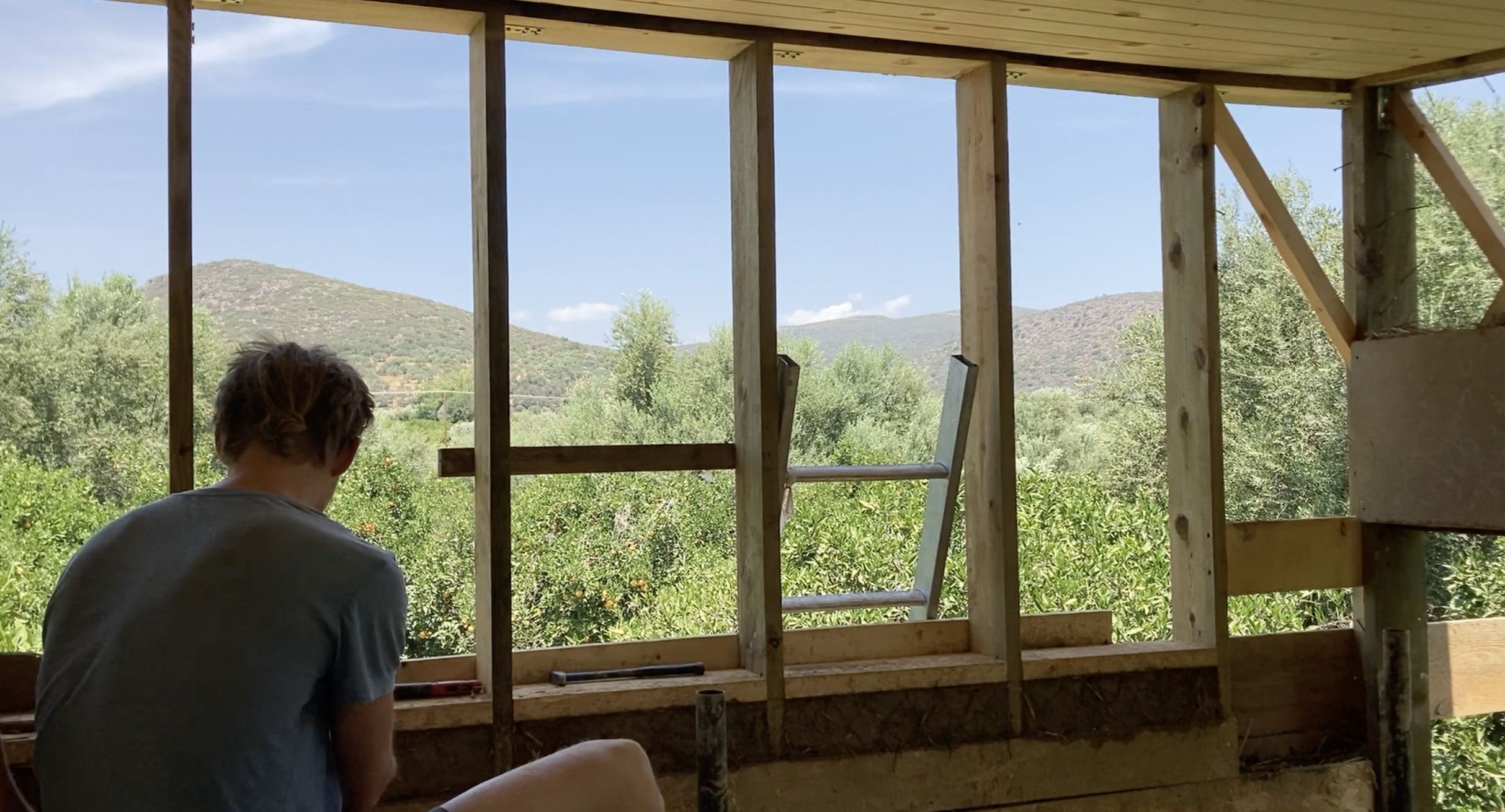 Une personne assise devant une ossature bois vitrée ouverte sur les collines