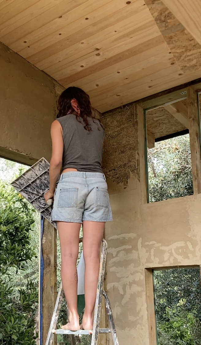 Une participante monte à l'échelle sous le plafond en bois du mini habitat