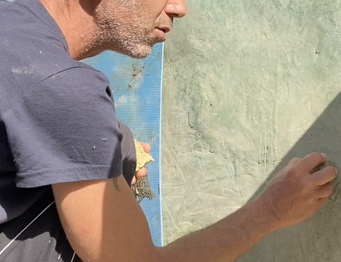 Un participant polit un mur au tadelakt vert-de-gris, à la main
