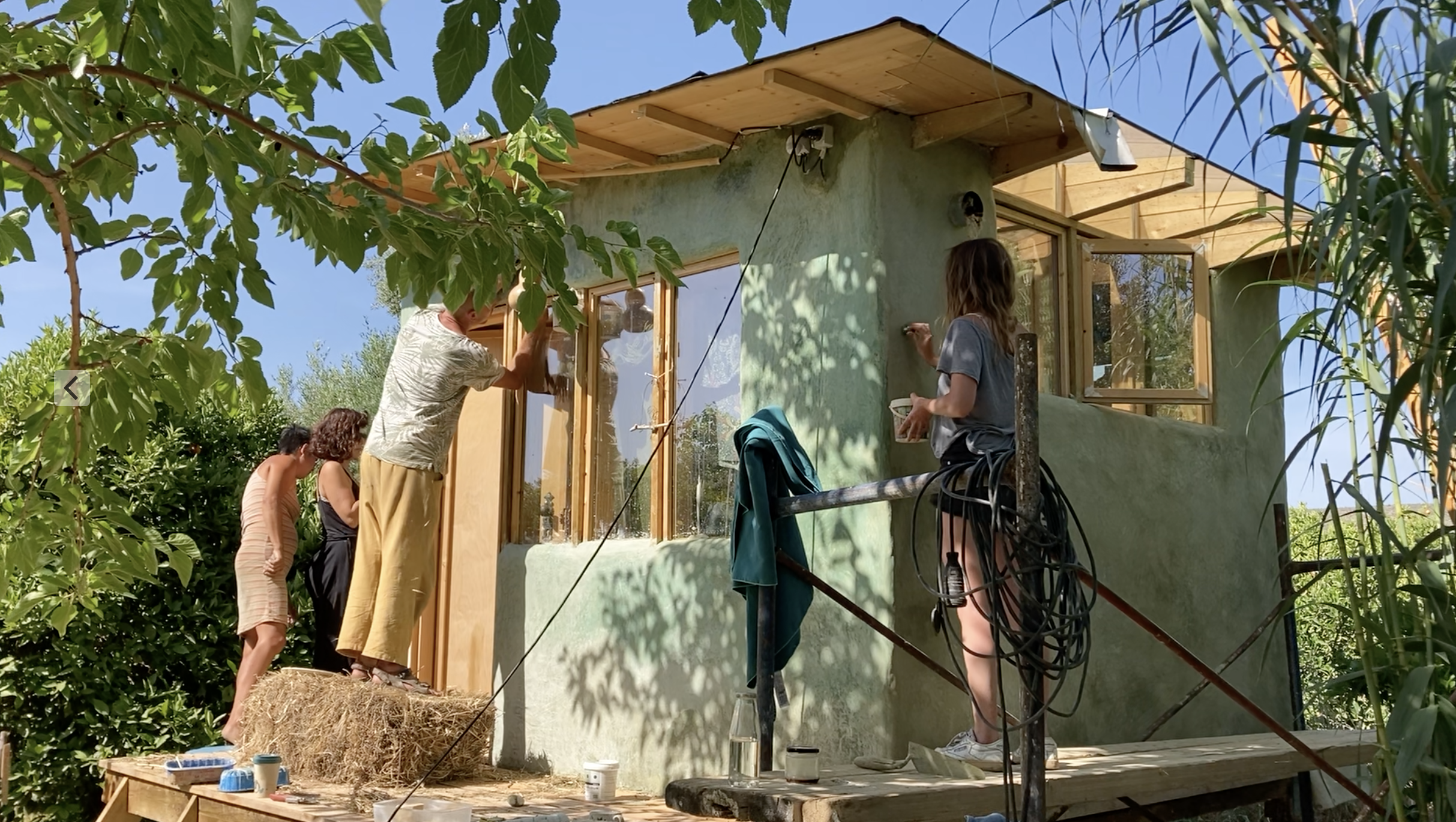 Deux participants enduisent la façade du mini habitat entouré de roseaux