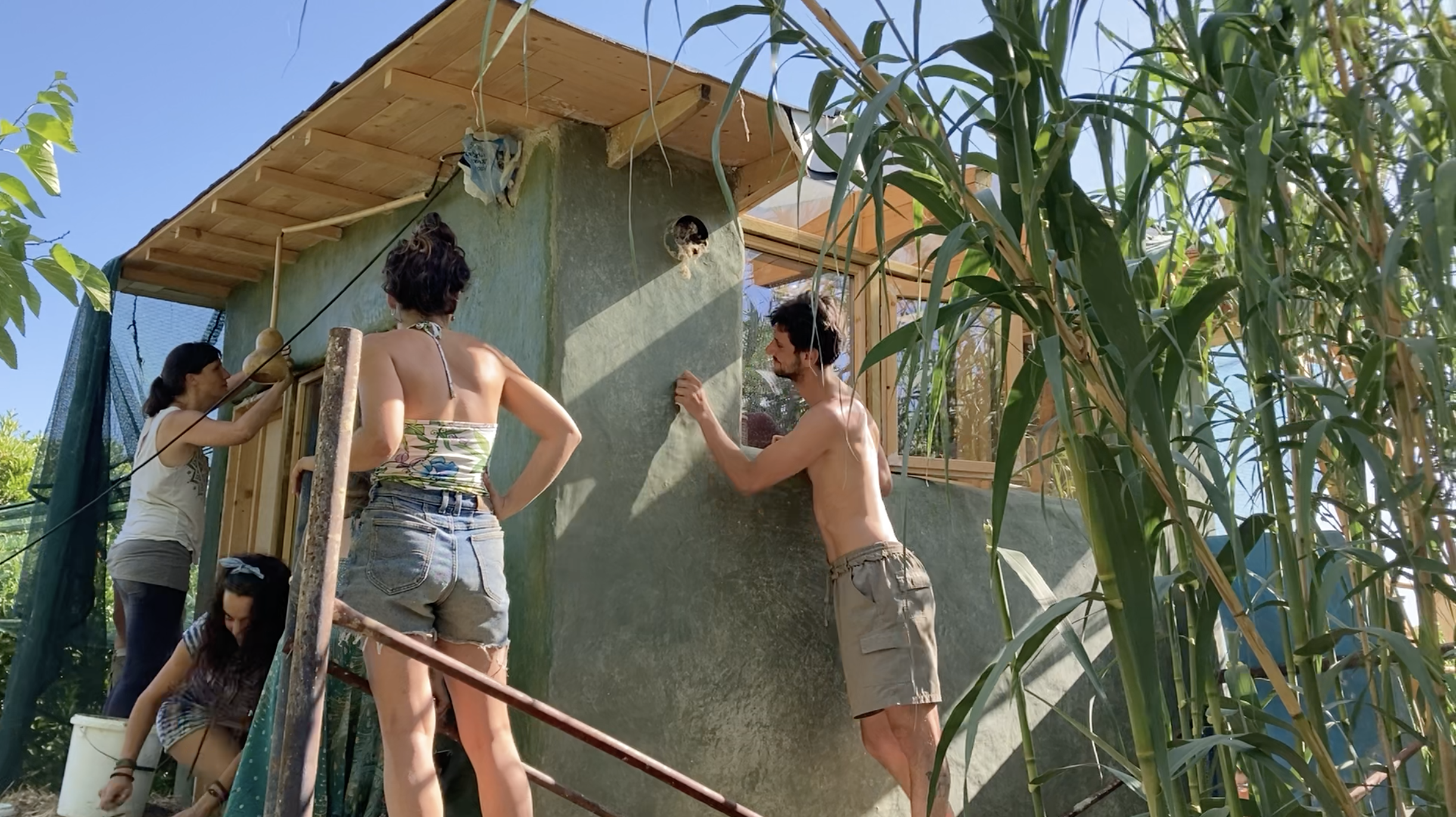 Trois participants travaillent la façade du mini habitat au soleil