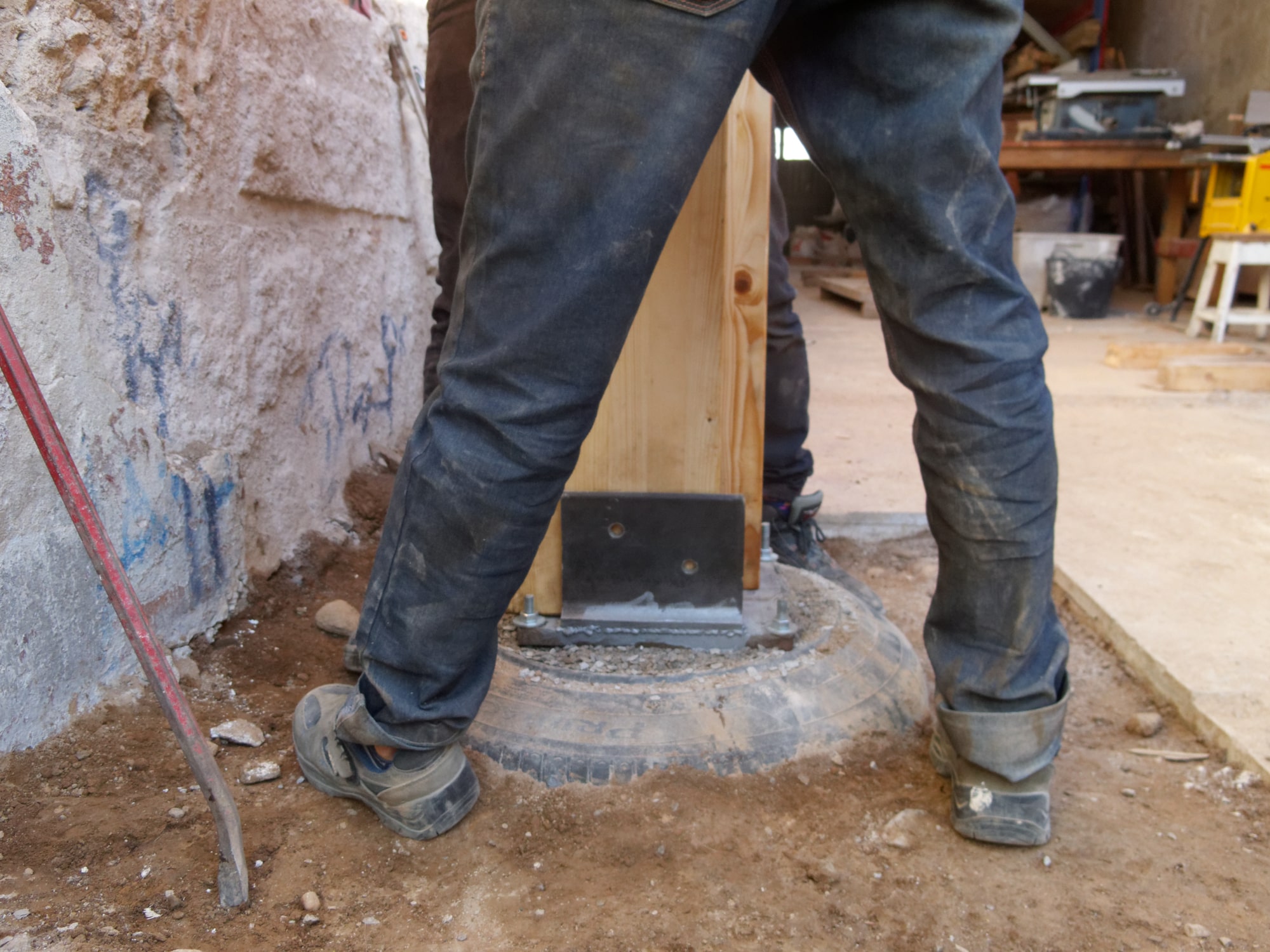 Poteau bois calé sur un pneu rempli servant de fondation