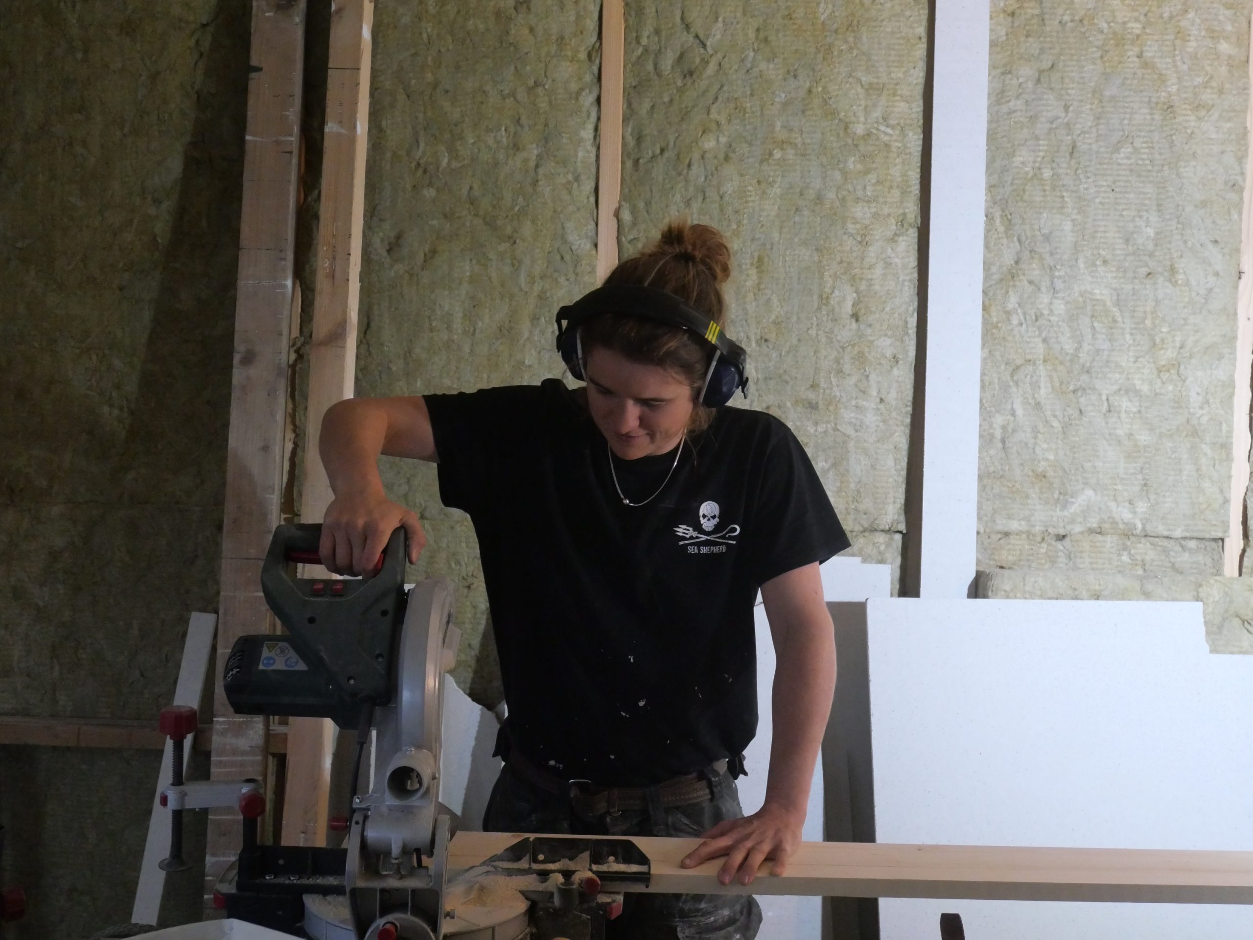 Une participante découpe une plaque à la scie, casque antibruit