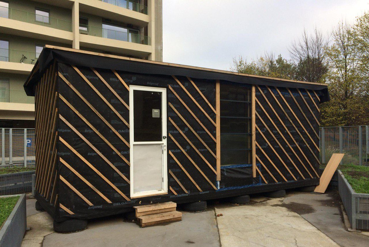 Le pavillon terminé, bardage bois en losanges et porte blanche, au pied d'un immeuble