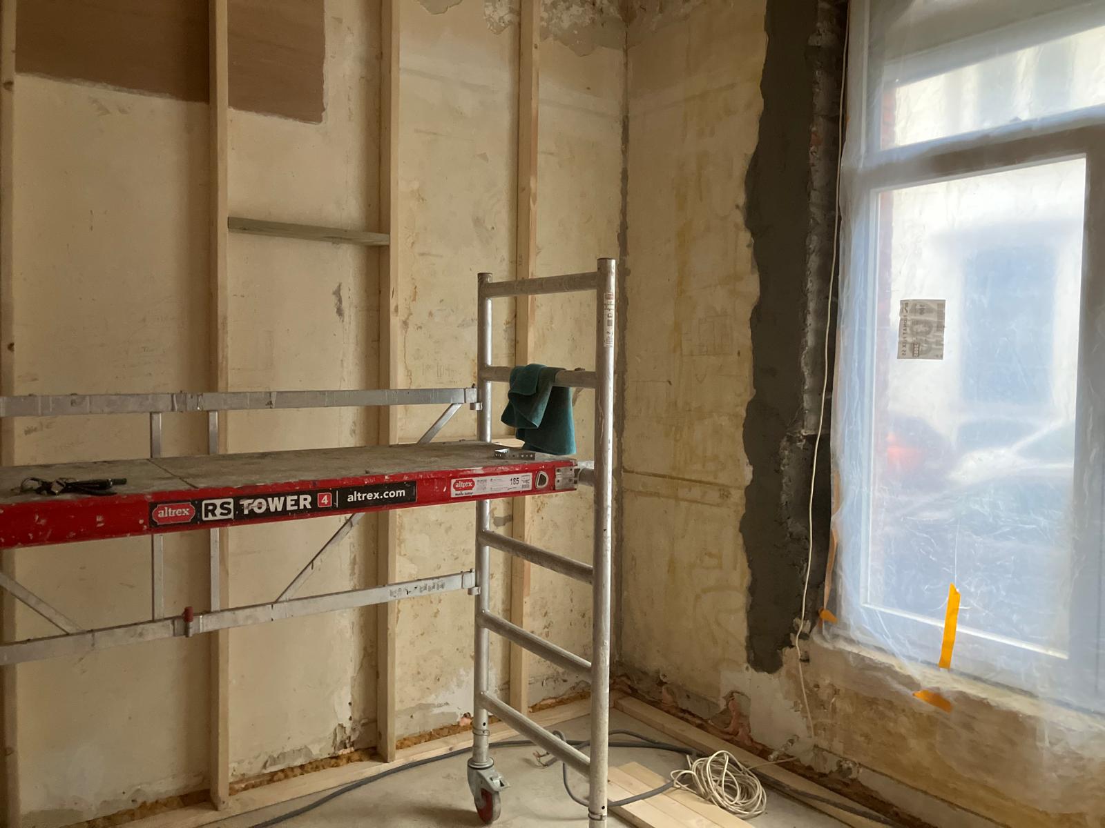 Mur décapé près d'une fenêtre, échafaudage et niveau posés