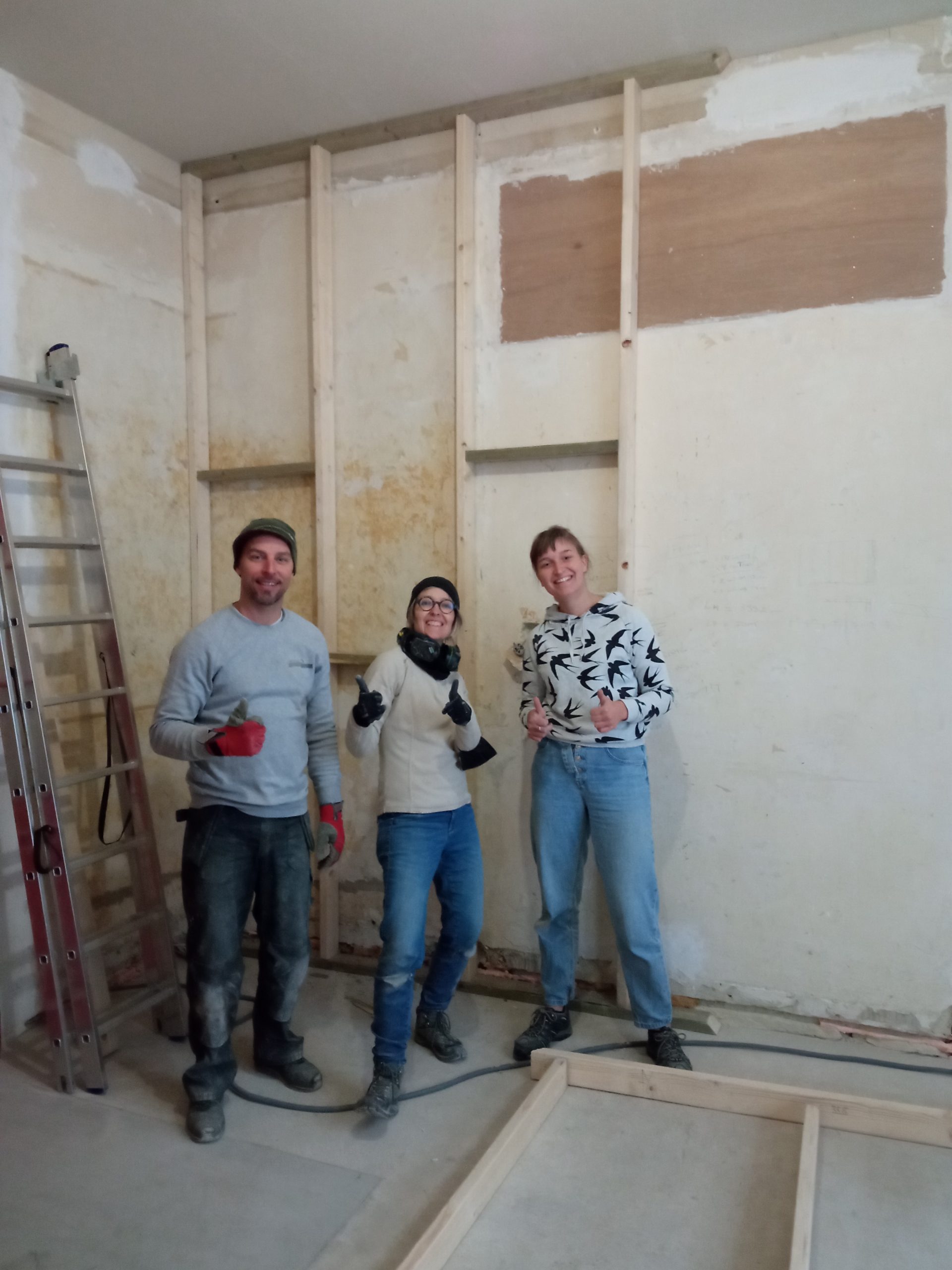 Trois participants posent dans la pièce en chantier