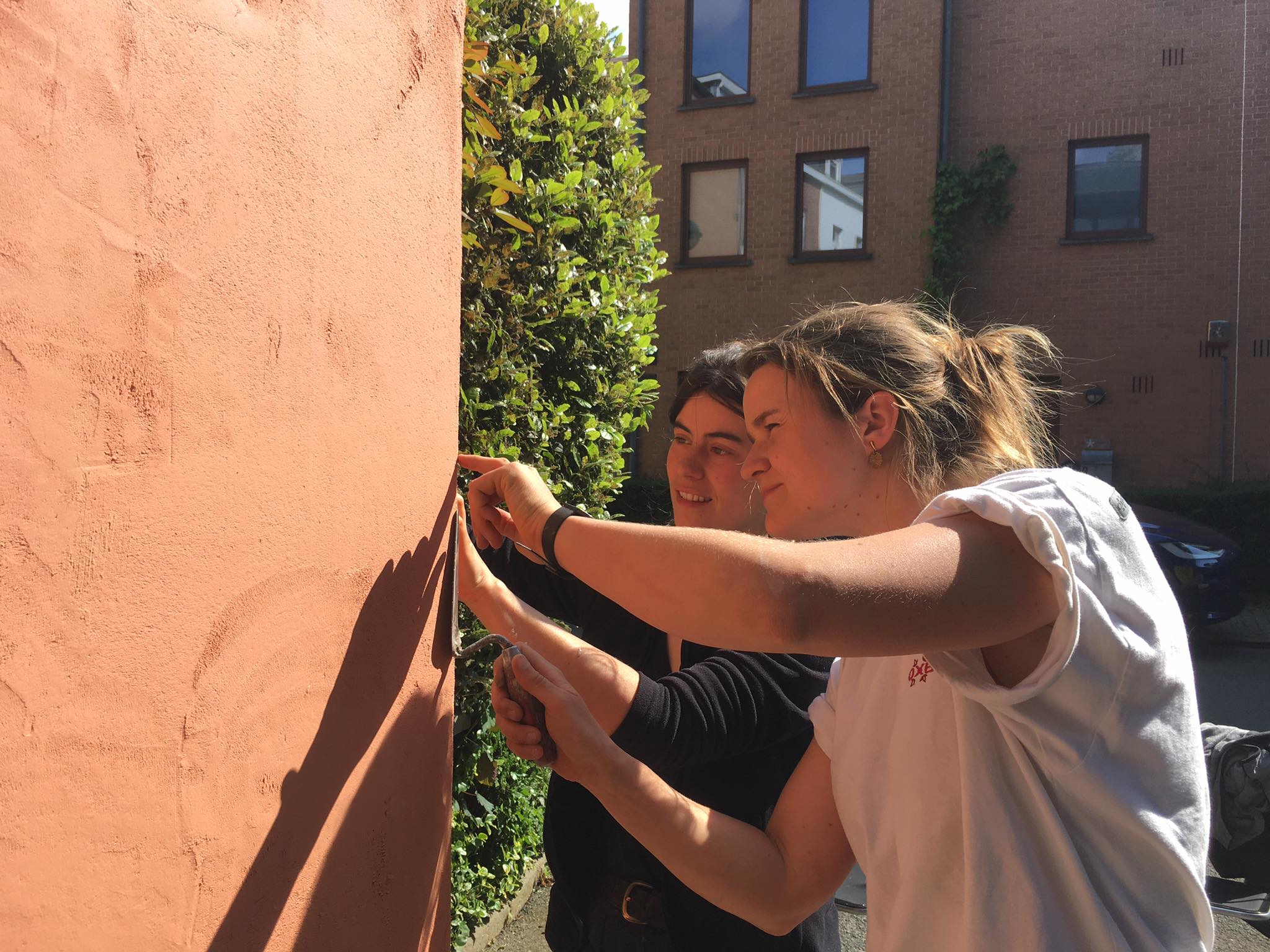 Deux participantes lissent l'enduit ocre sur un panneau, en plein soleil