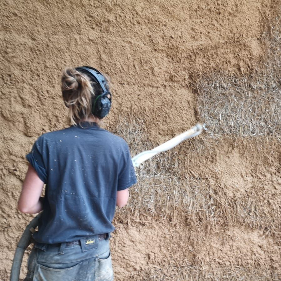 Une participante applique l'enduit sur un mur en paille, vue de dos