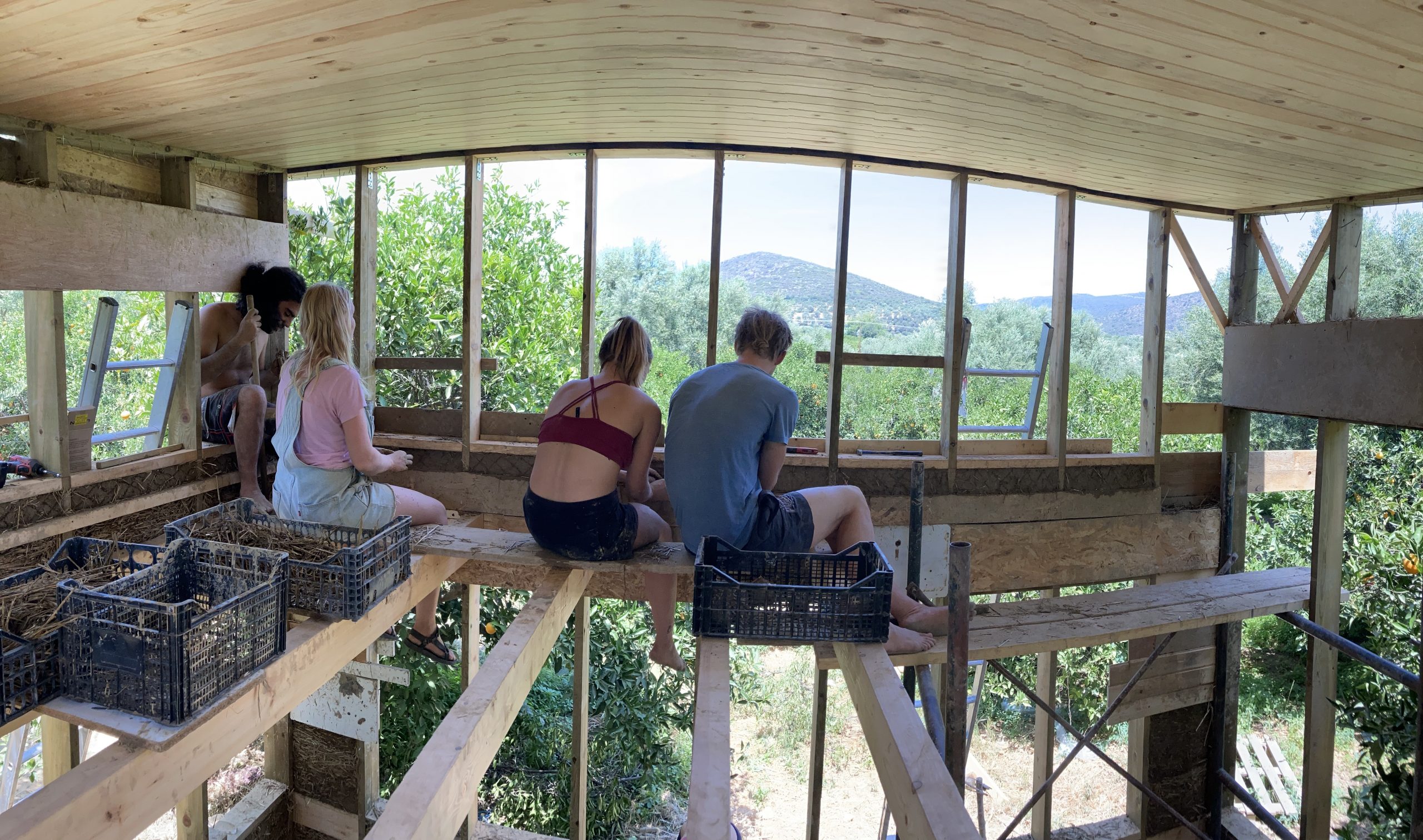 Groupe assis sur le balcon en bois du mini habitat, vue sur les collines