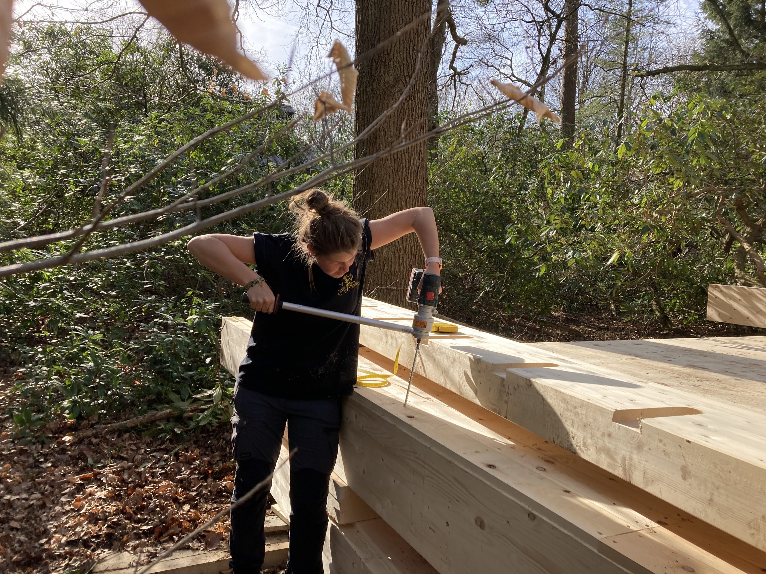 Une participante scie un montant bois debout sur le chantier en forêt
