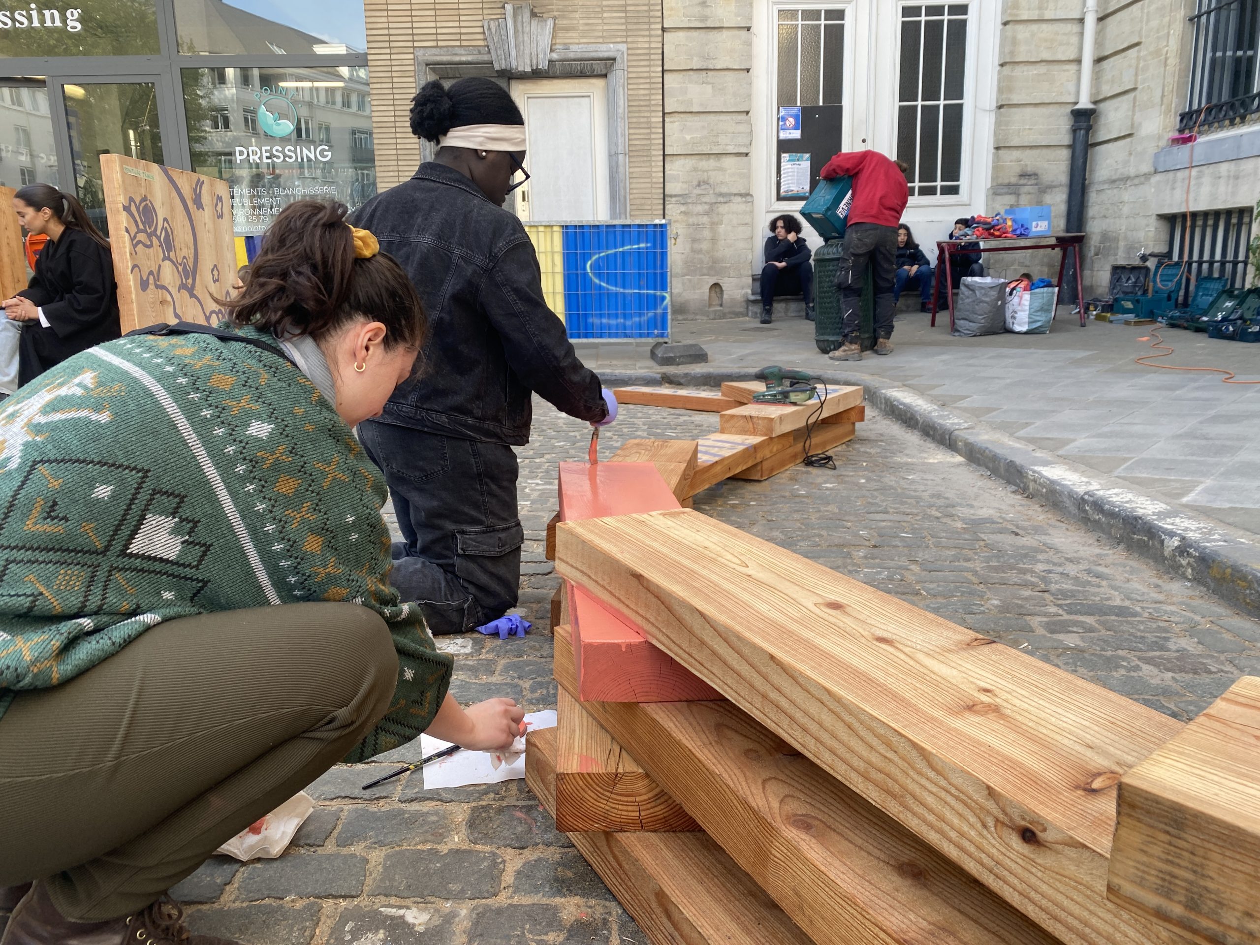 Deux participants assemblent une banquette en bois sur la rue pavée