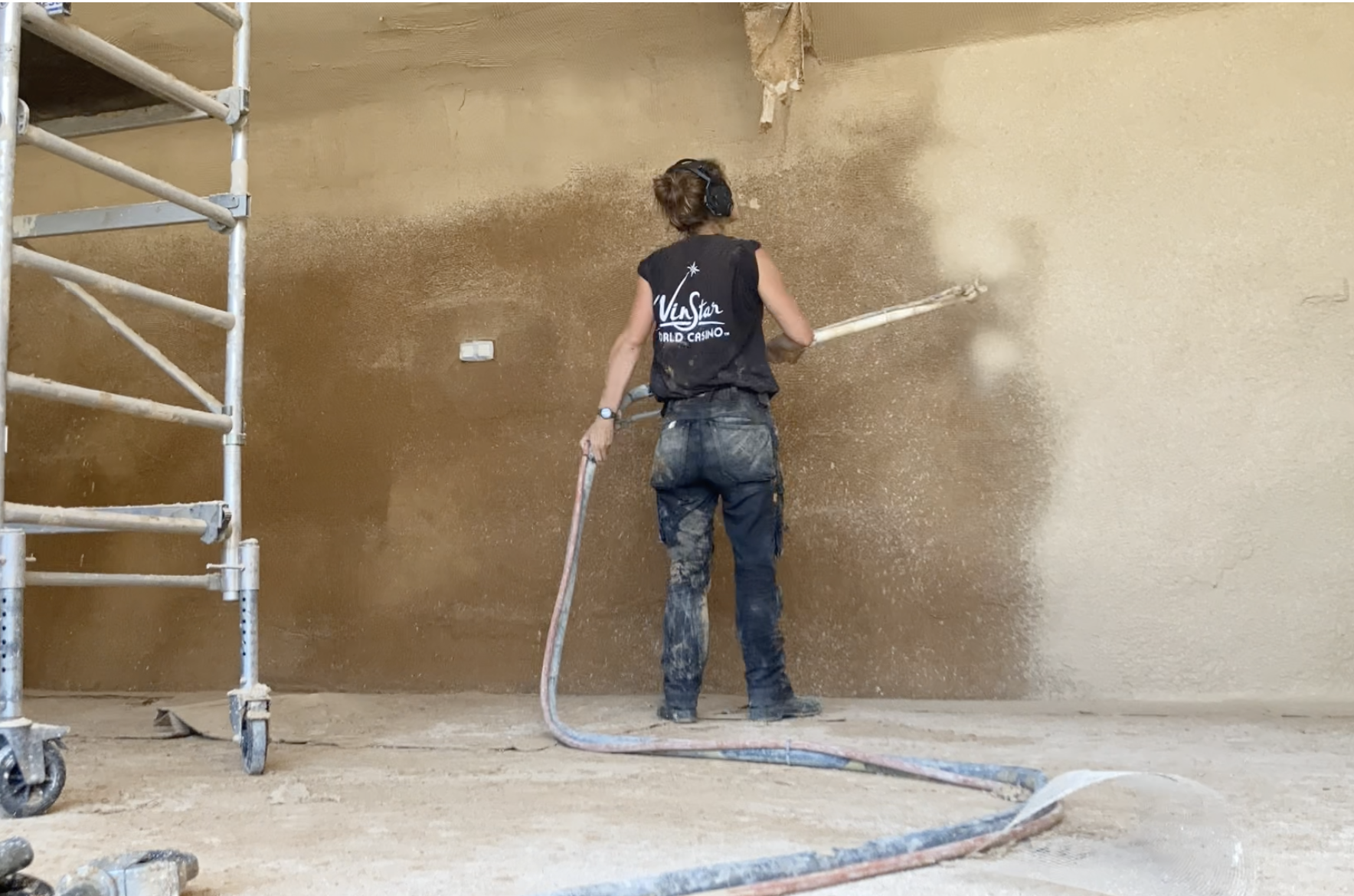 Une participante projette l'enduit en argile au mur, depuis un échafaudage roulant