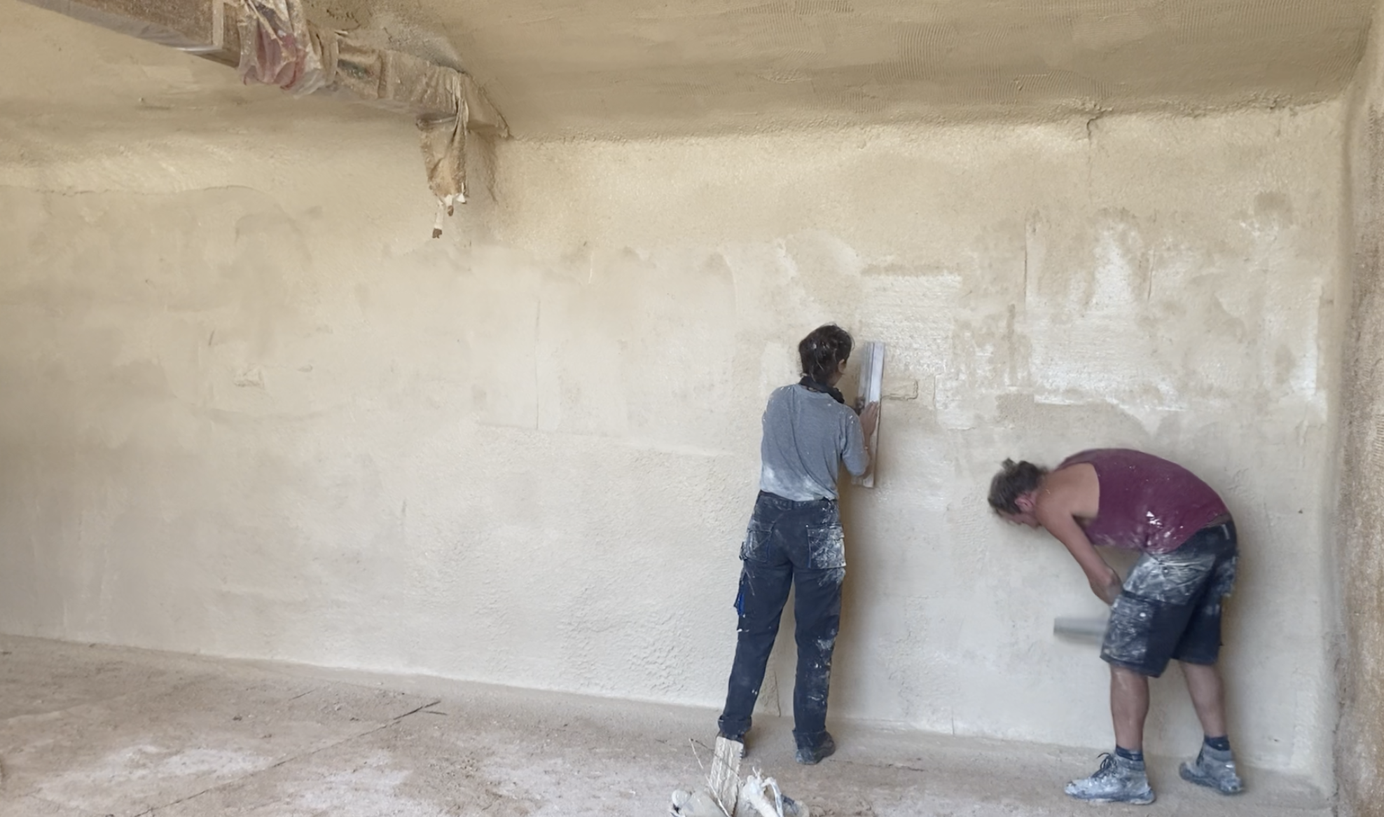 Deux participants lissent un grand mur enduit en terre crue