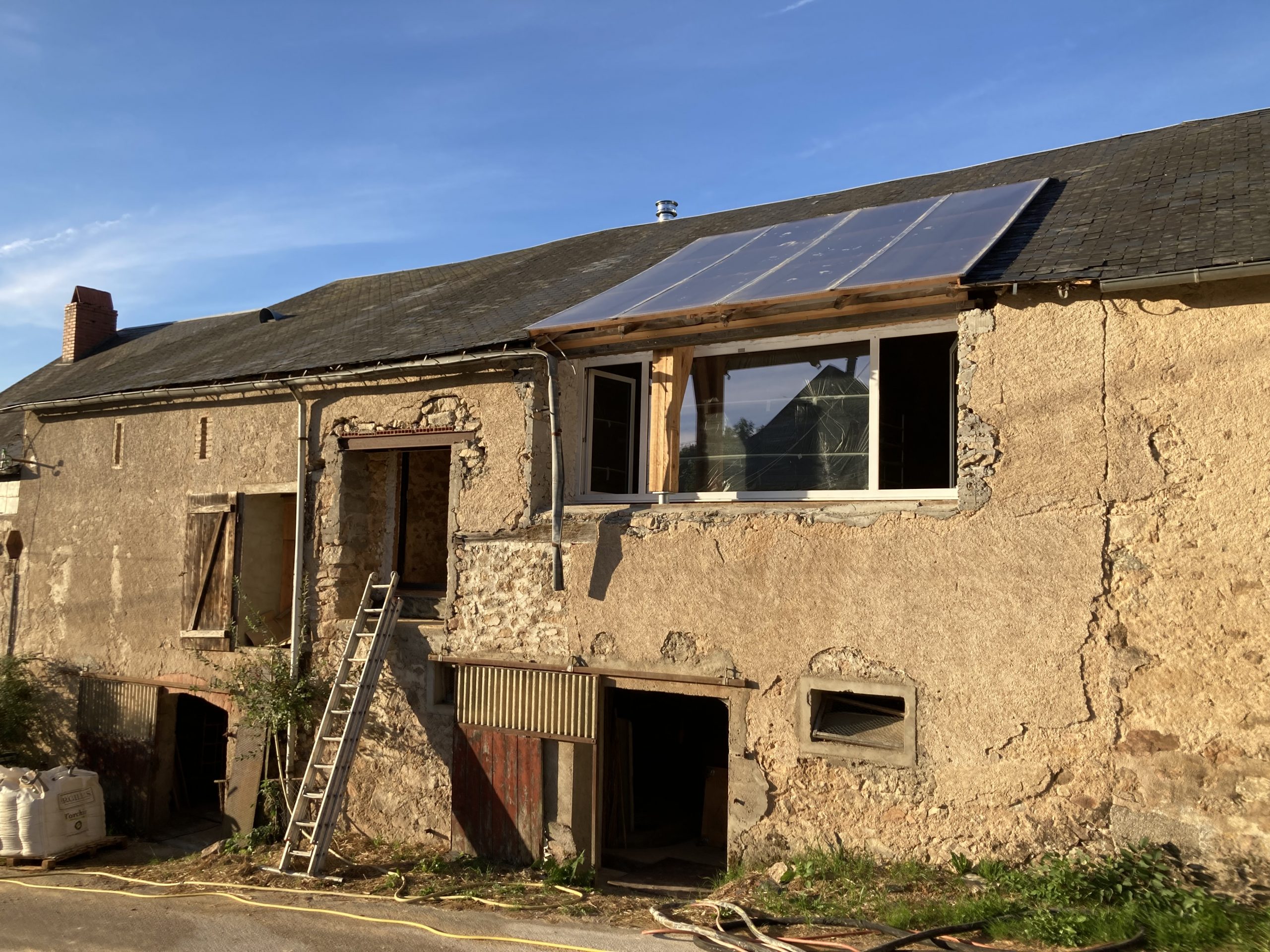 Façade de l'ancienne ferme en pierre avec panneaux solaires en toiture