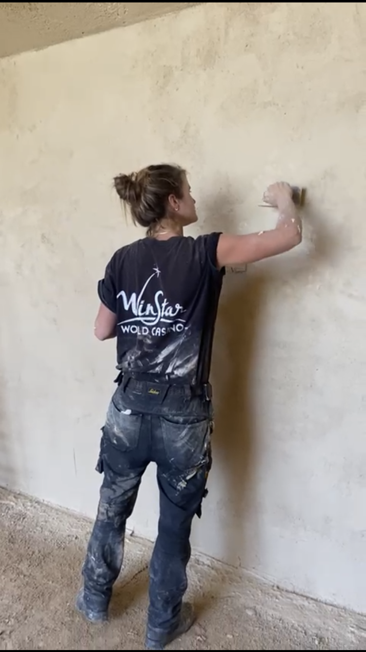 Une participante lisse un mur en terre crue, vue de dos