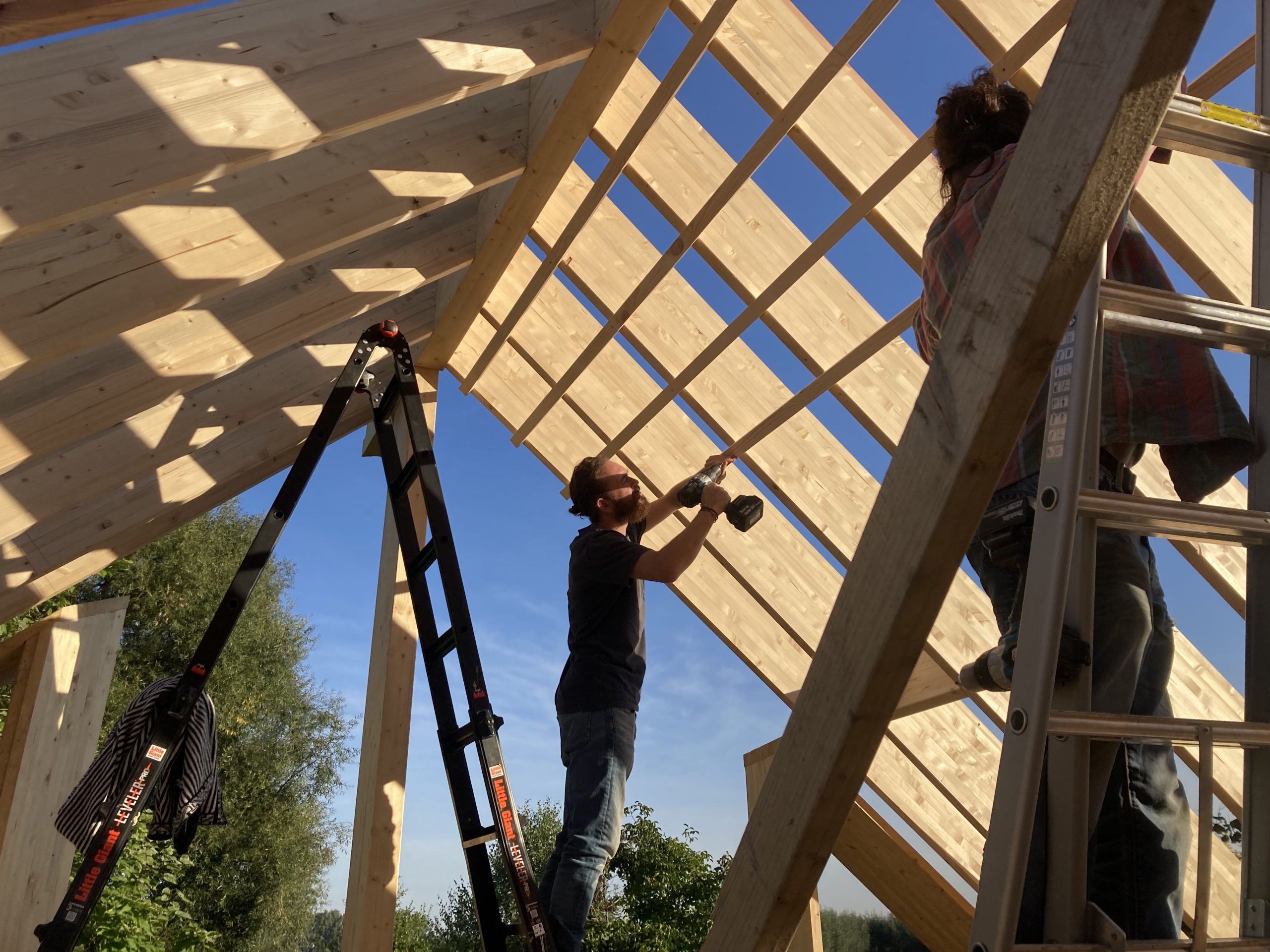 Participants travaillant sur la charpente à claire-voie, échelles dressées