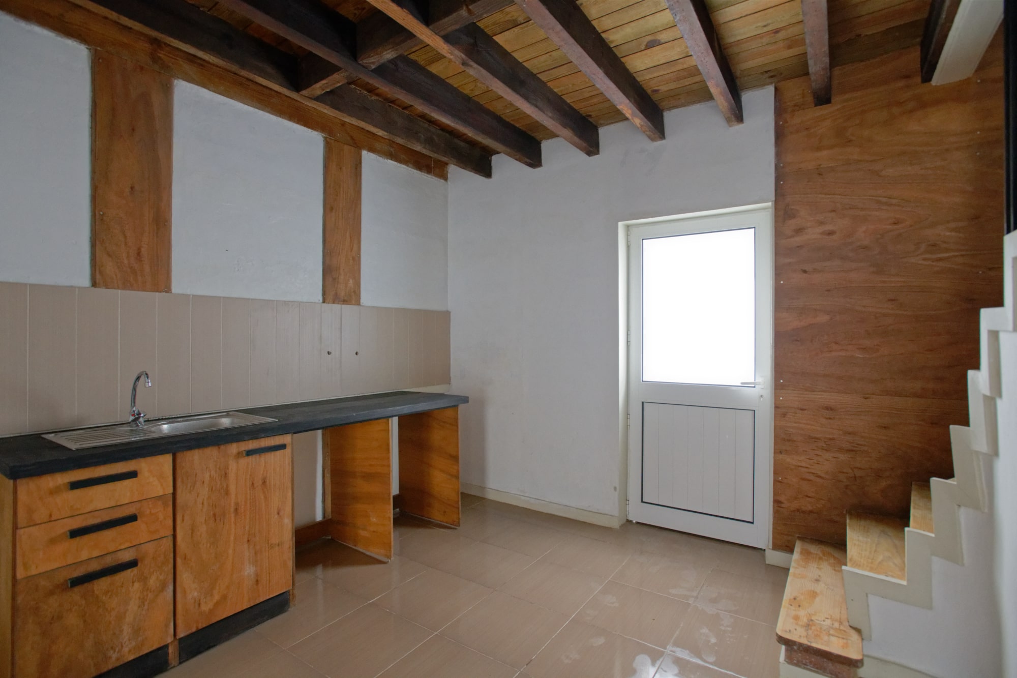 Cuisine rénovée en bois avec escalier blanc et plafond à poutres