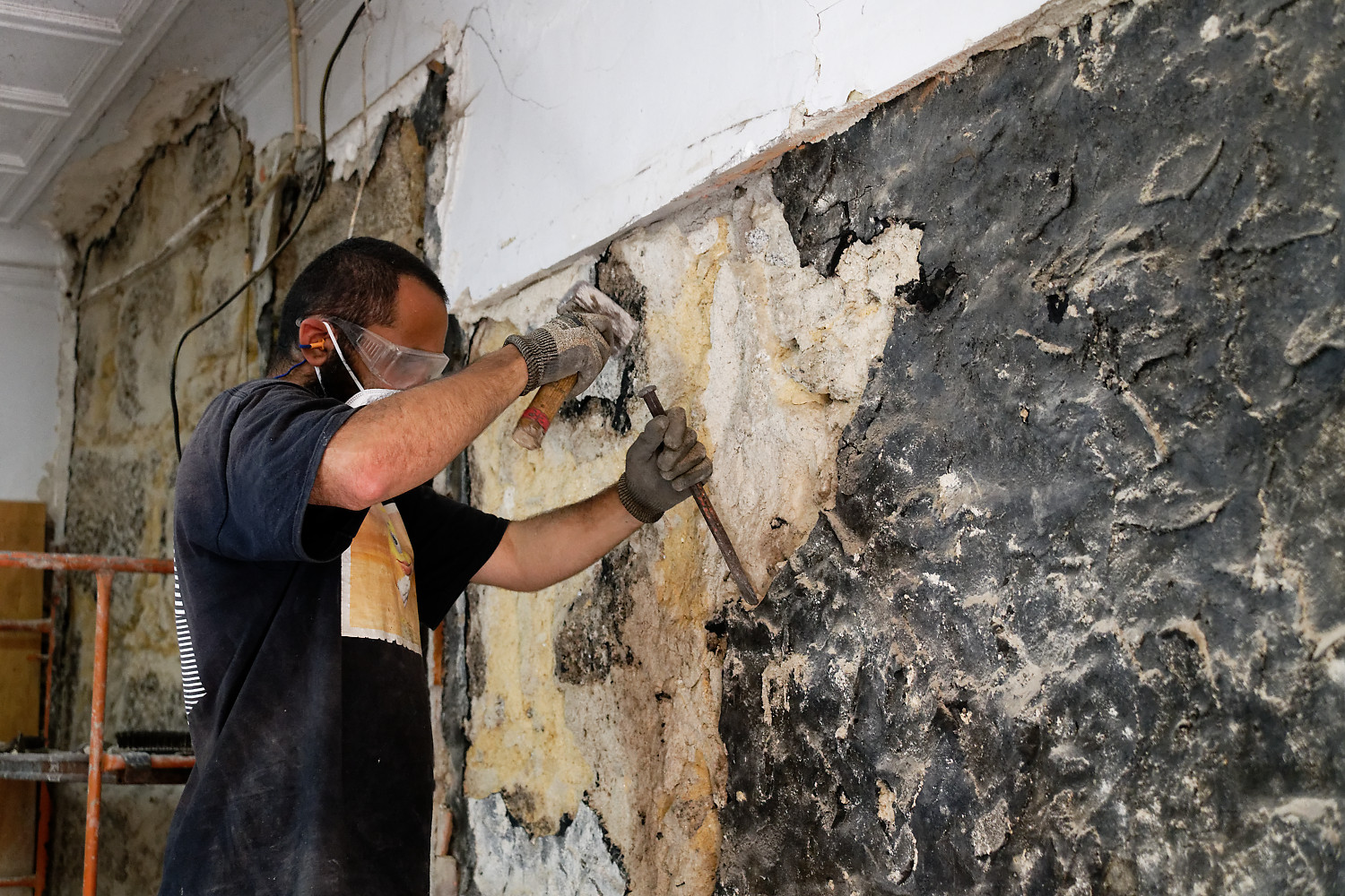 Un participant masqué répare un mur en granit à la truelle