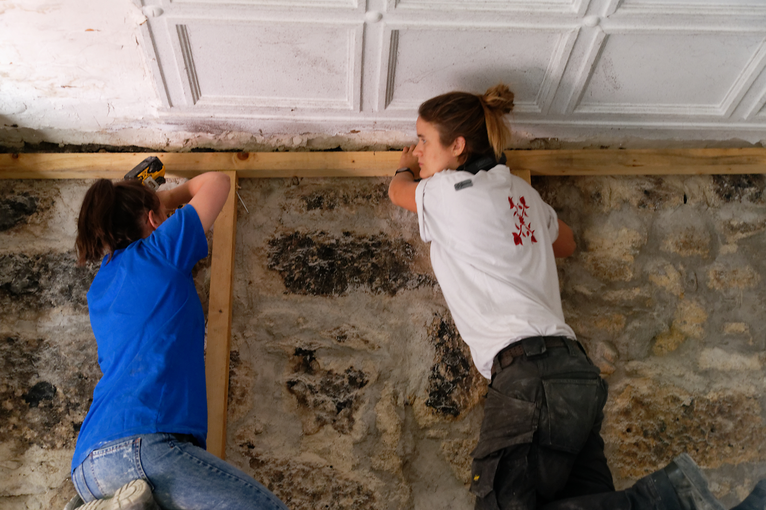 Deux participants fixent une ossature bois contre le mur en granit