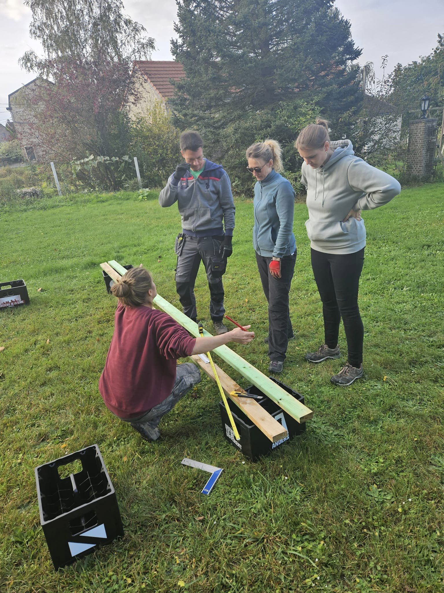 Participants mesurant et sciant des montants bois sur l'herbe