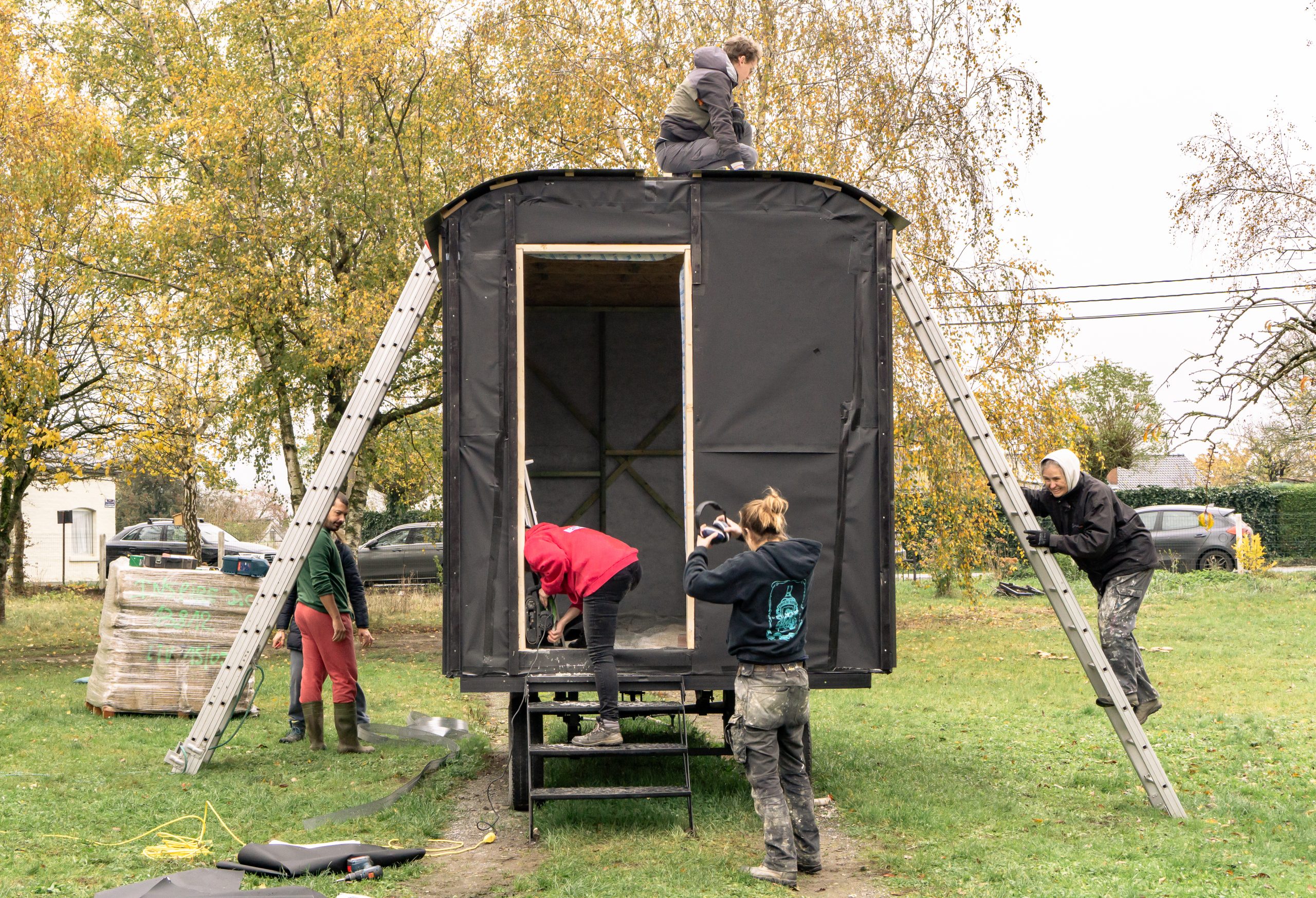 Roulotte en construction, participants sur des échelles autour de la caisse
