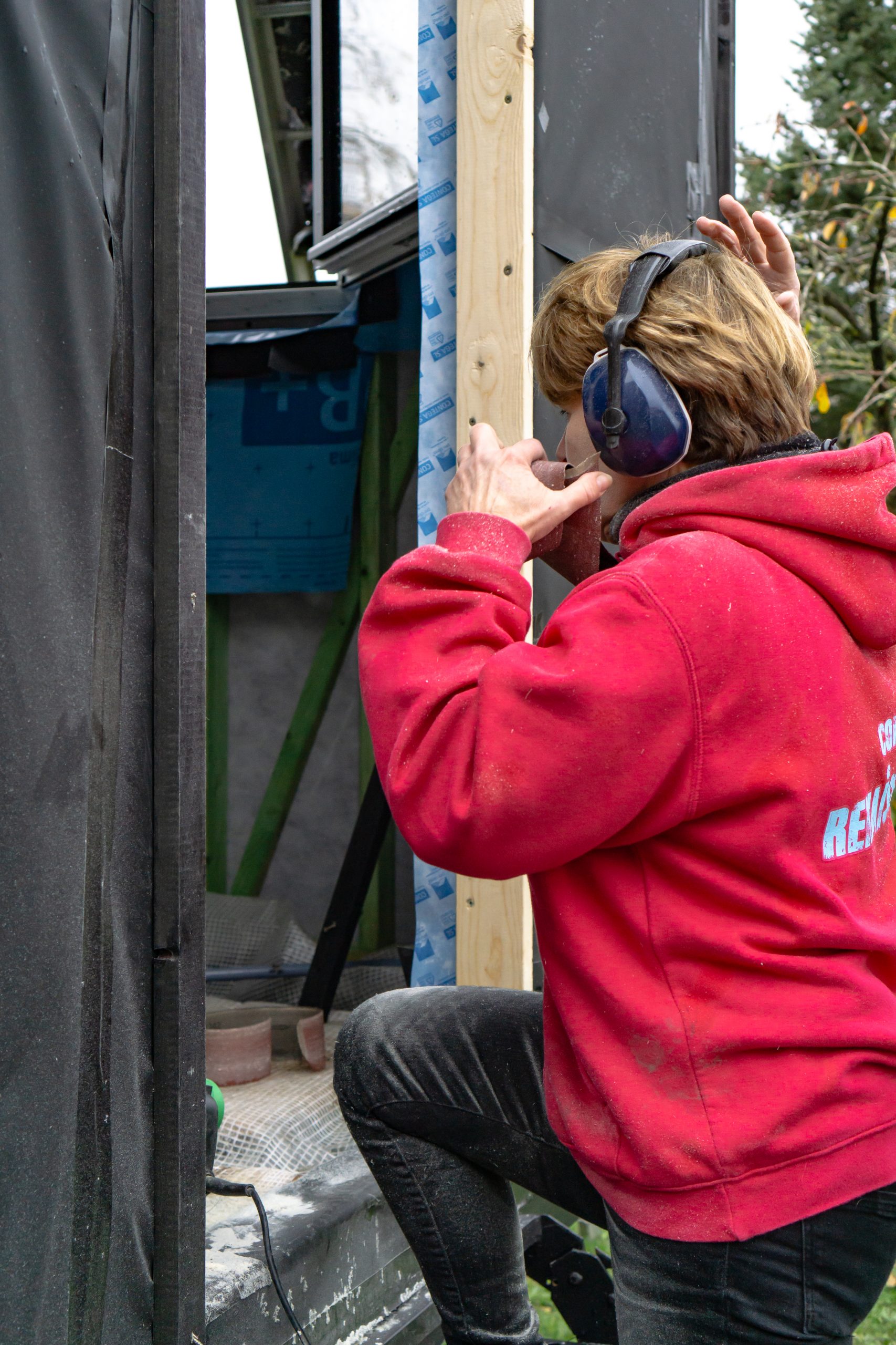 Une participante en sweat rouge découpe une pièce, casque antibruit