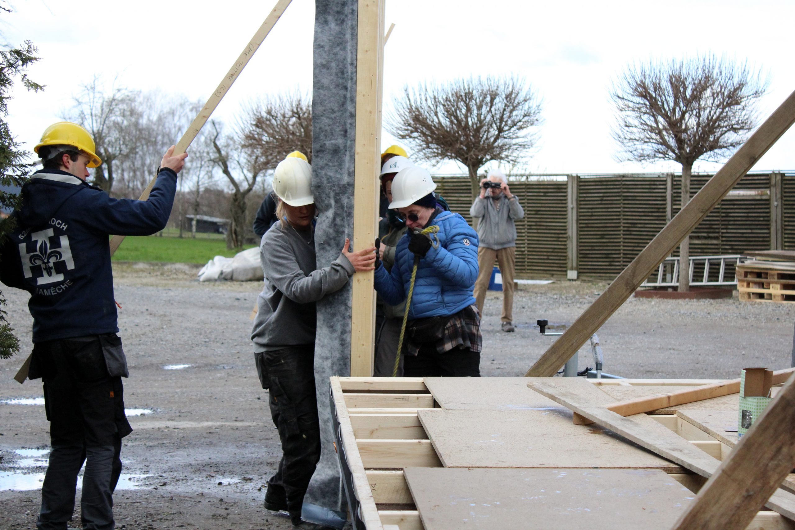 Plusieurs participants lèvent et calent un pan de mur en ossature