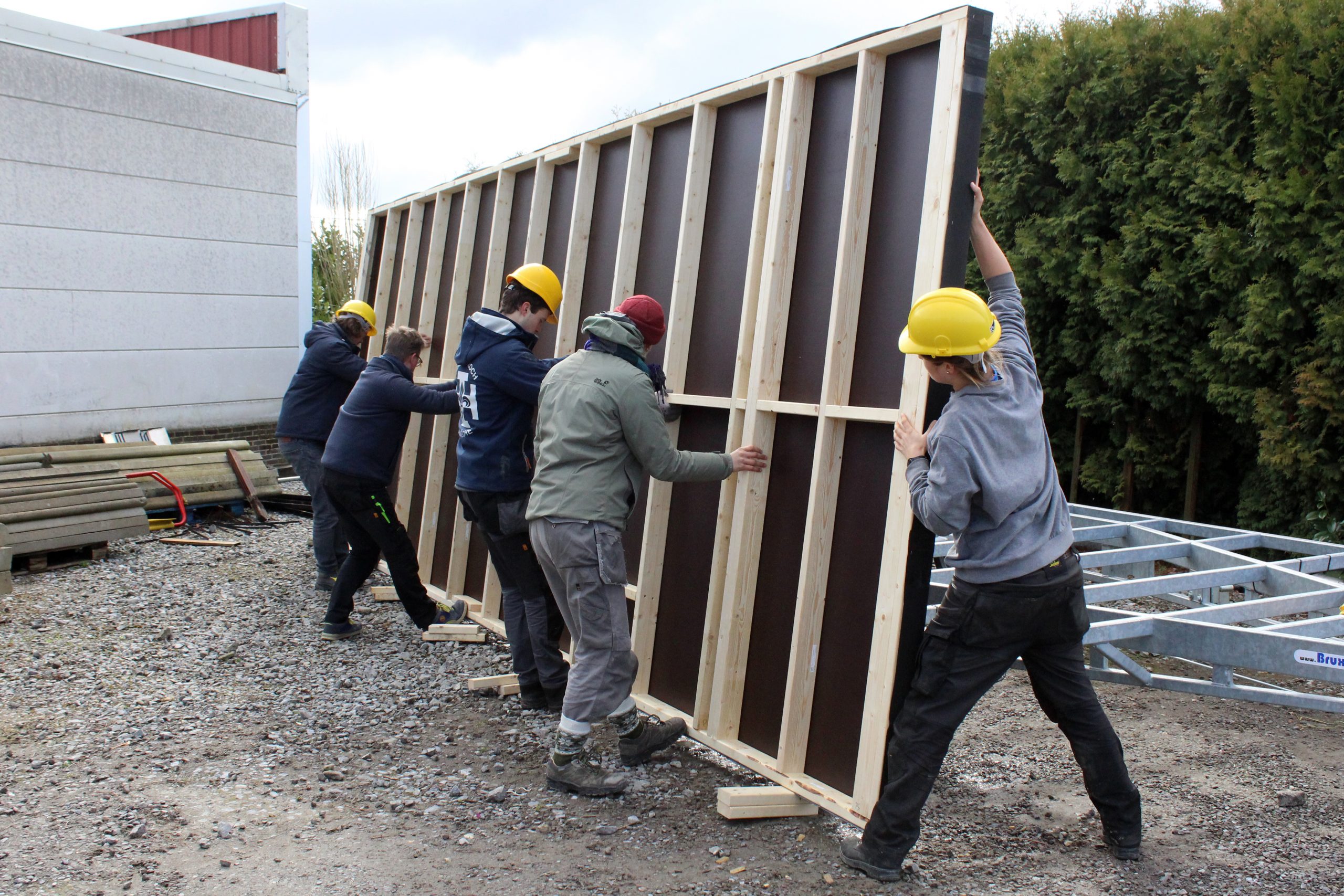 Plusieurs participants dressent un grand pan de mur contre le bâtiment