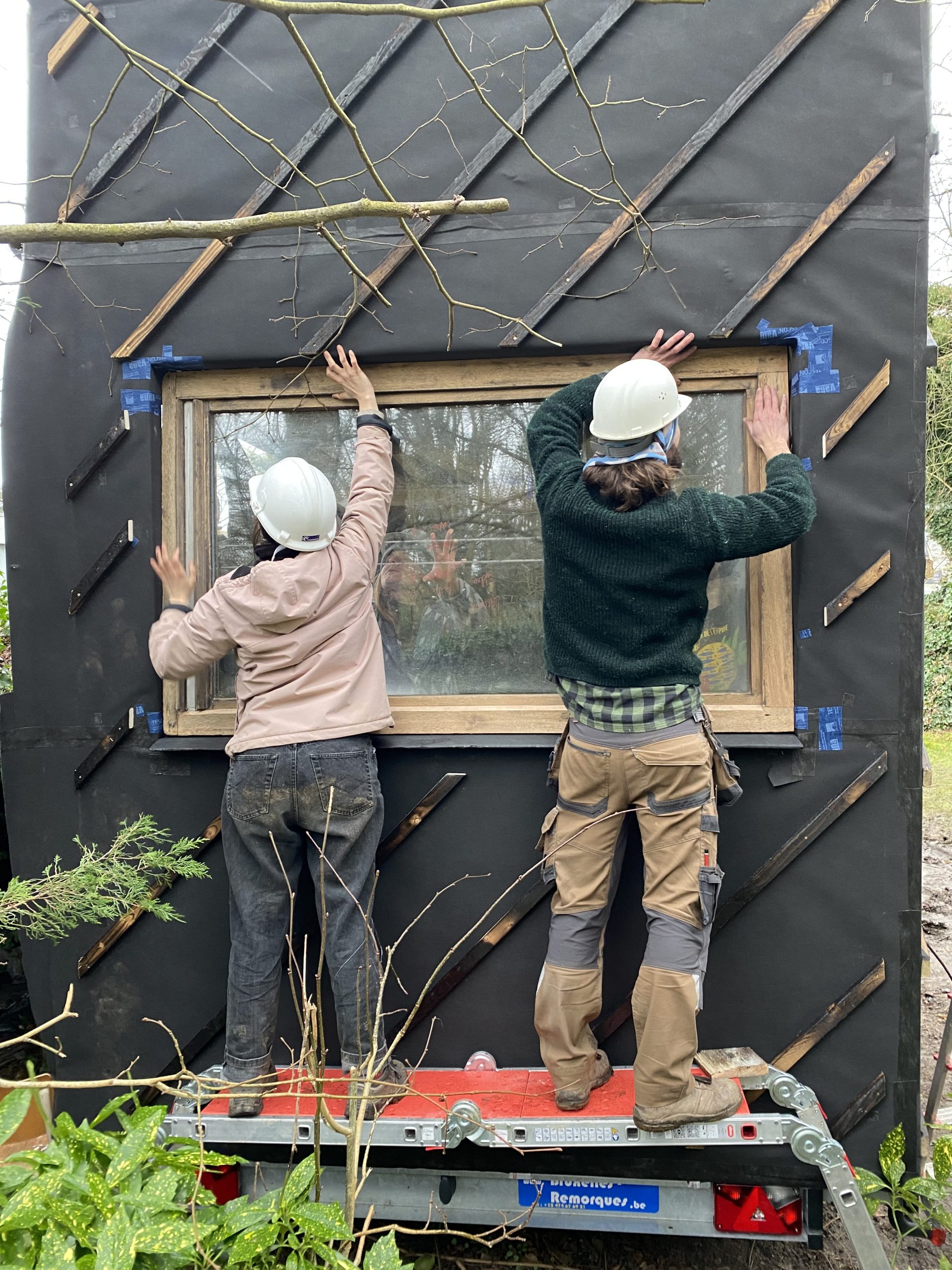 Deux participants posent une fenêtre sur le flanc de la tiny house