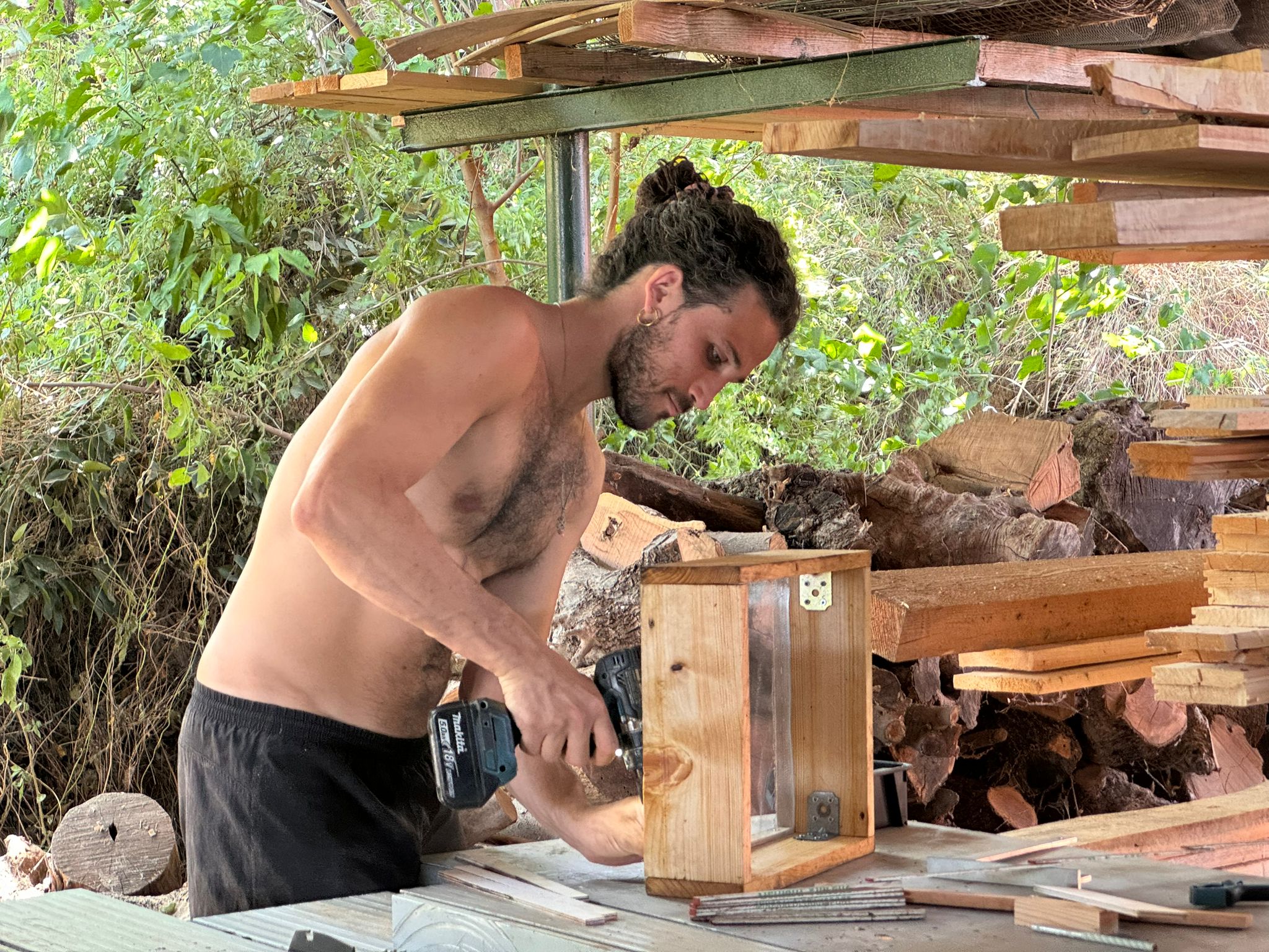 Un participant travaille un panneau bois sous un abri, en forêt