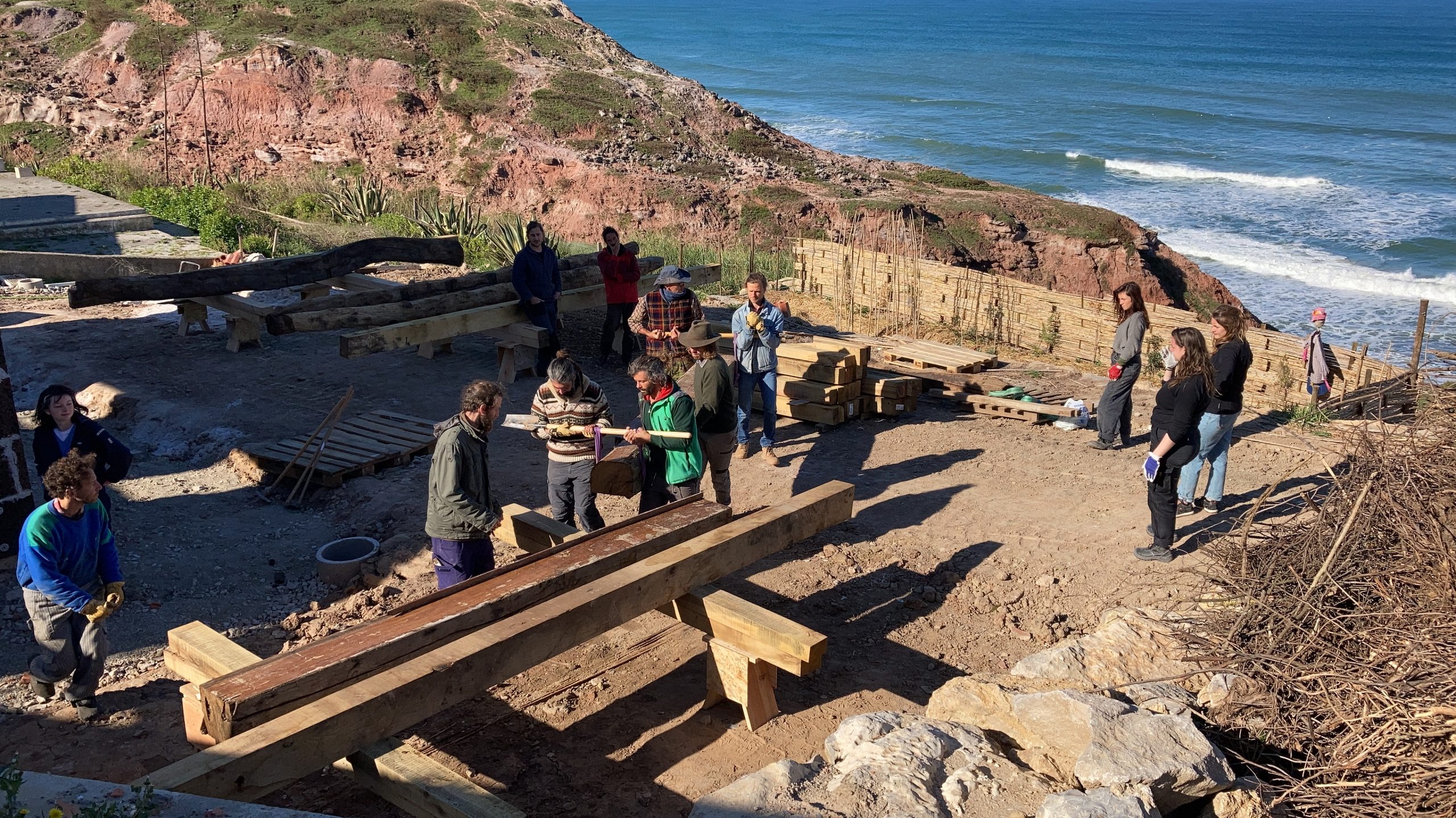 Participants travaillant le bois sur un site en bord de falaise, océan en fond