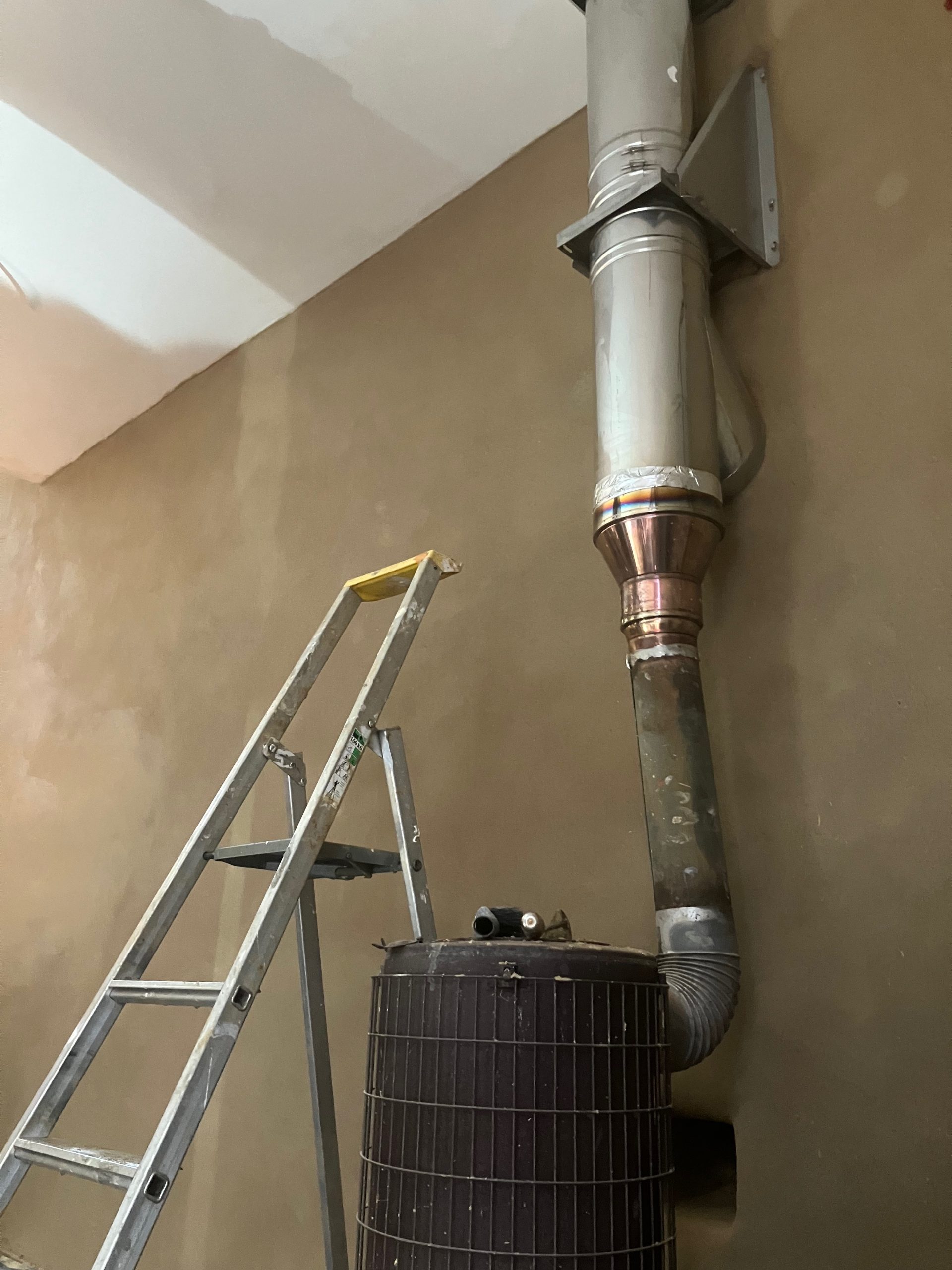 Conduit de poêle métallique le long d'un mur enduit en argile, escabeau à côté
